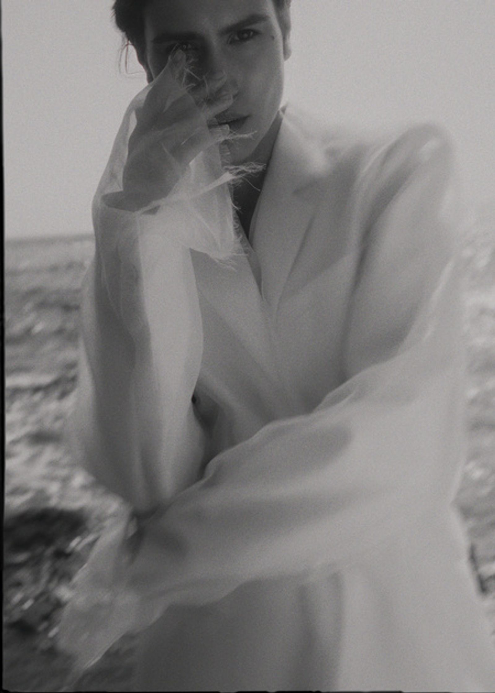 a woman in a white suit is posing by the ocean