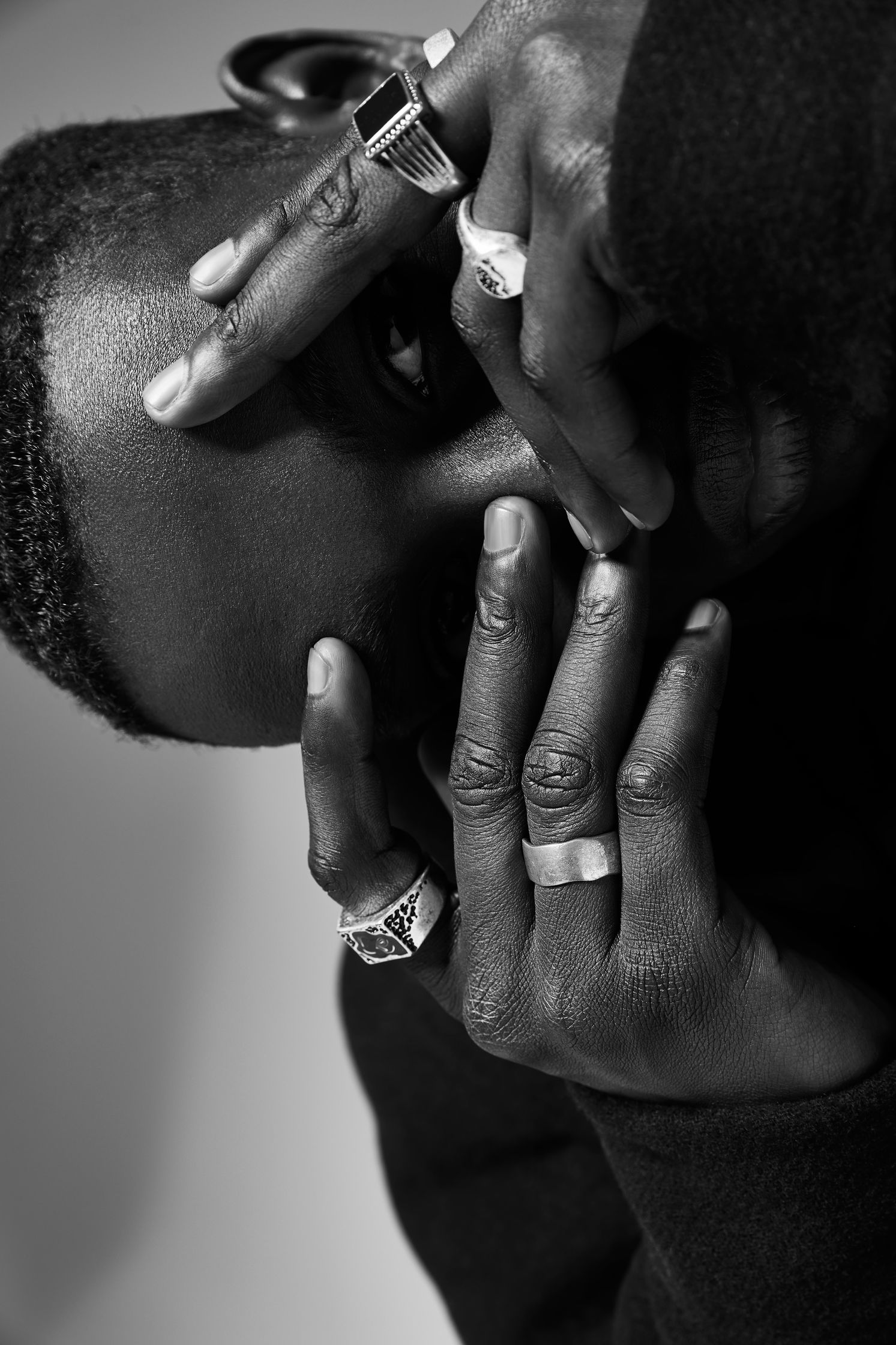 a black and white photo of a man covering his face with rings