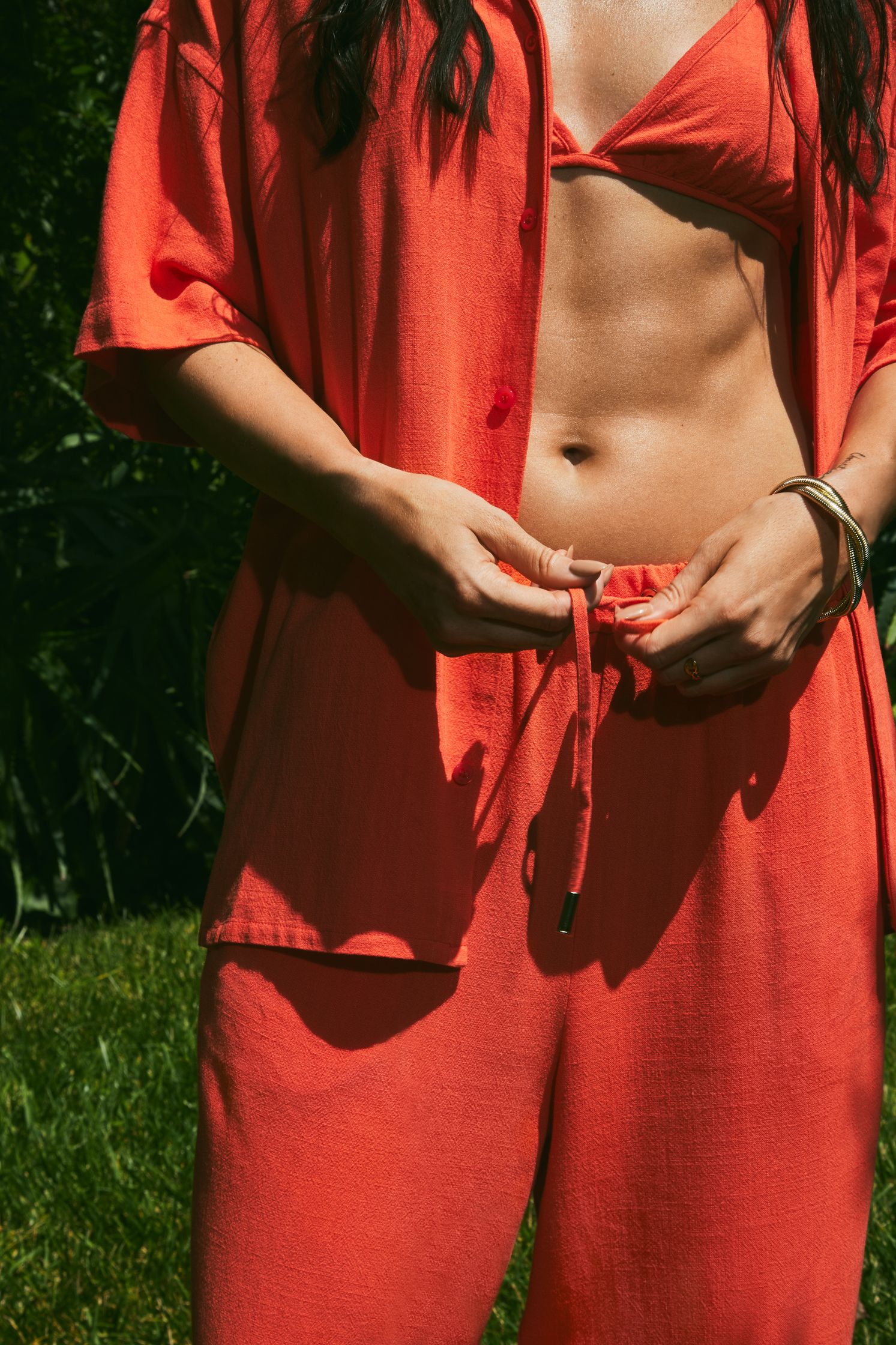 a woman in a red top and pants posing in the grass