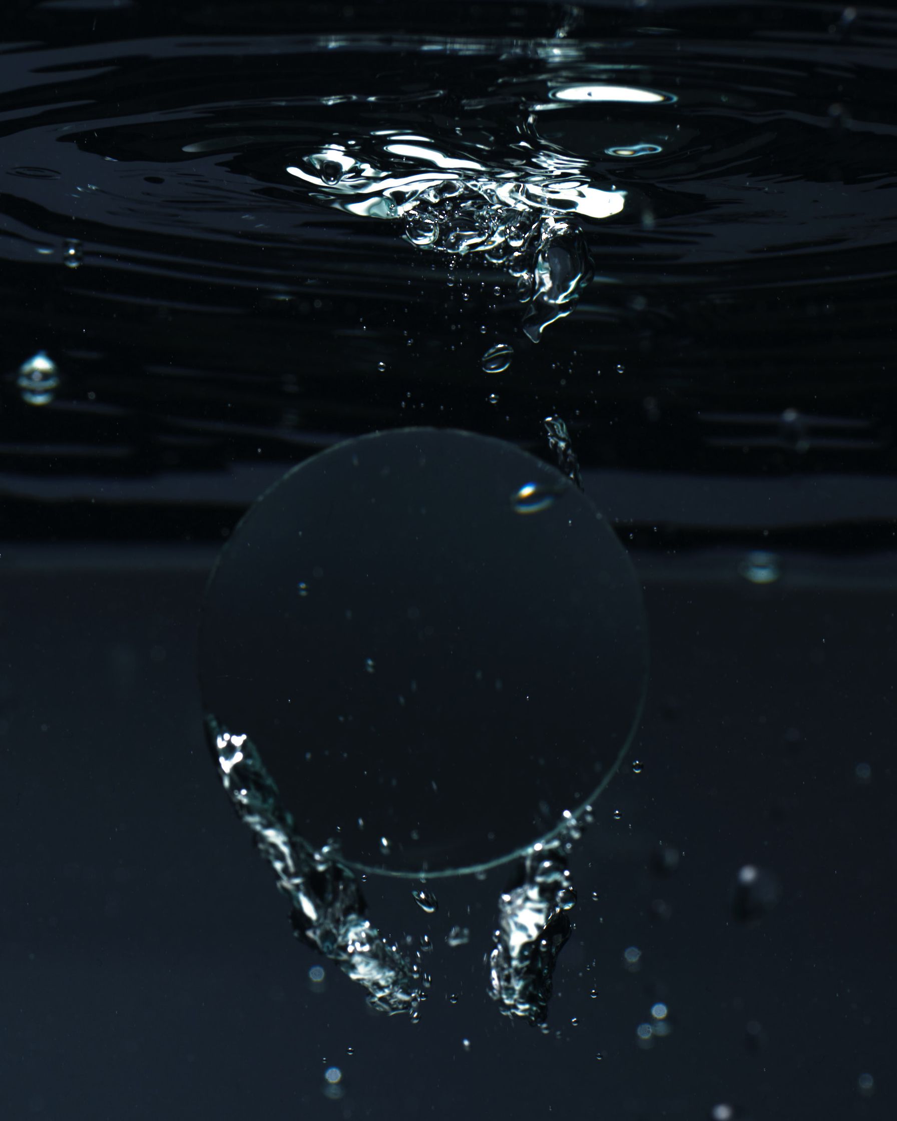 Abstract view of a convex glass disc as it enters water, with dynamic splash and ripple effects.