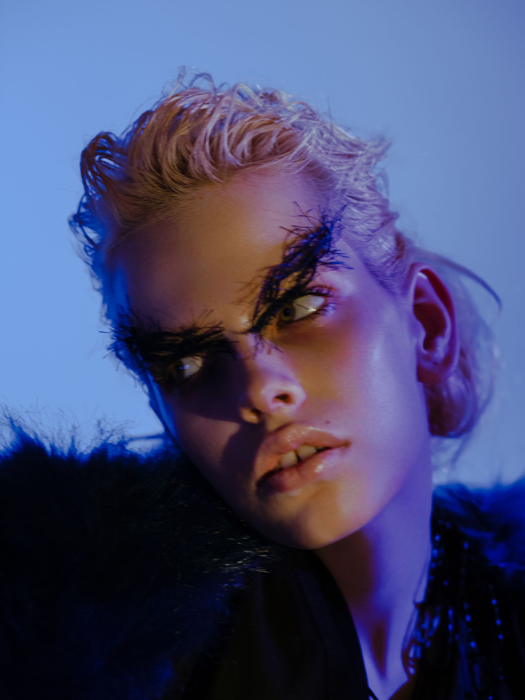 a woman in a fur coat and feathers is posing in front of a blue background