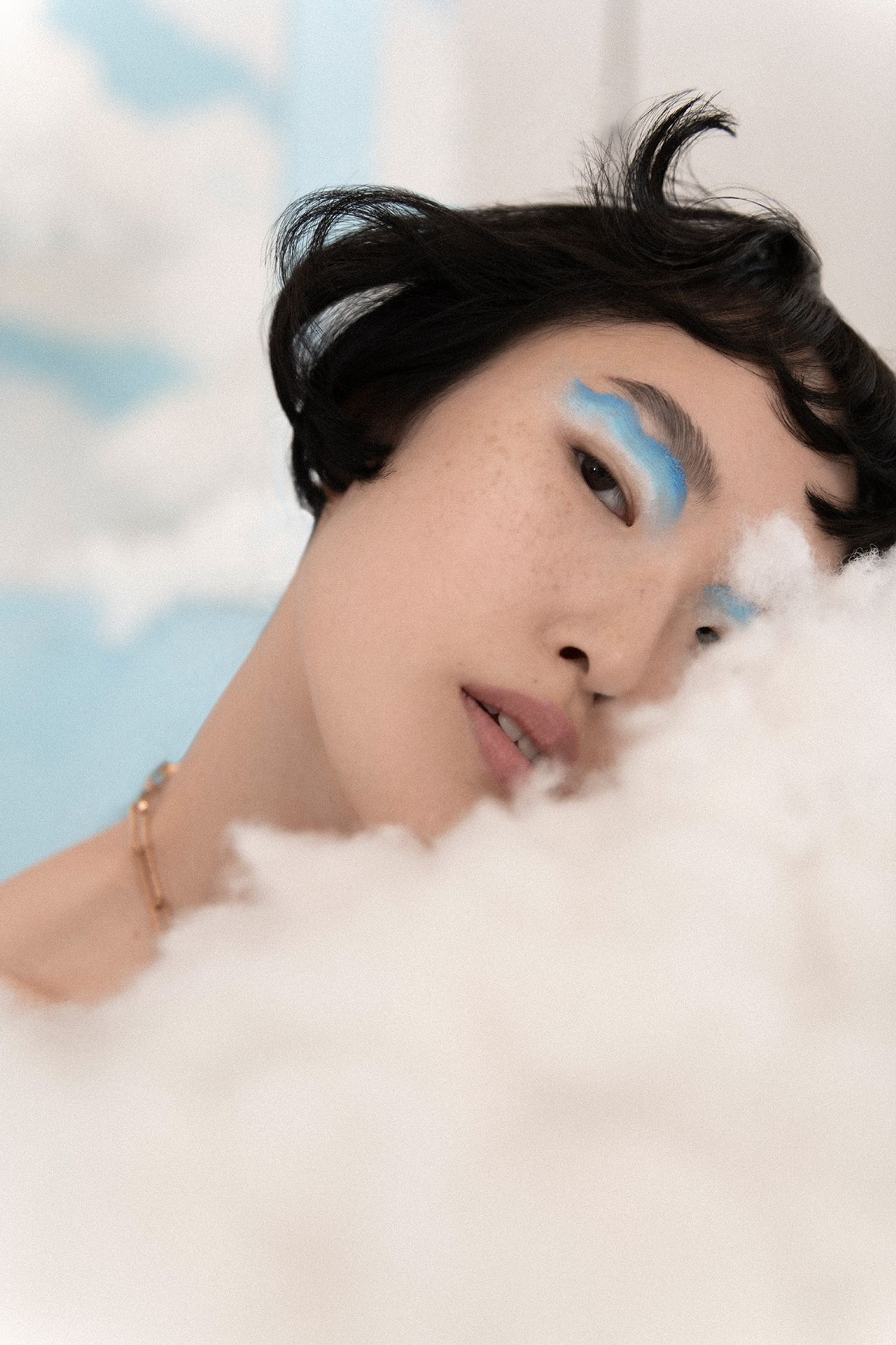 a woman laying on a cloud with blue eye makeup