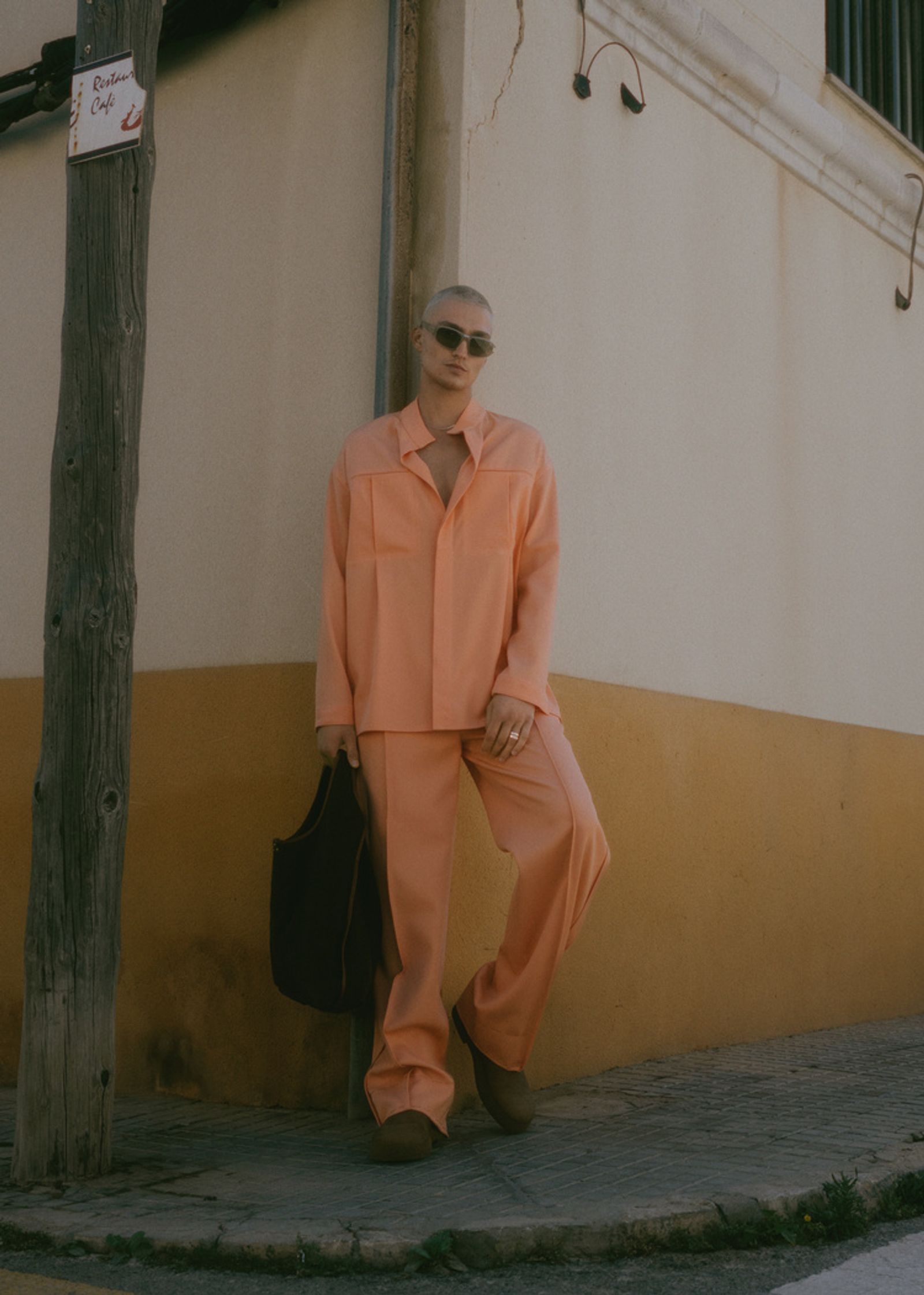 a woman in an orange suit leaning against a wall