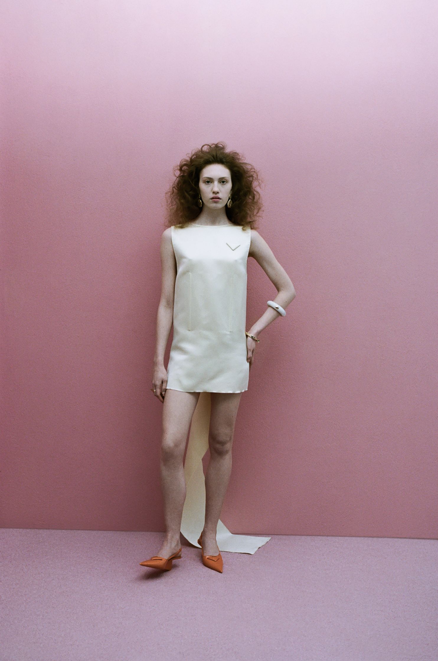 a woman in a white dress posing against a pink wall