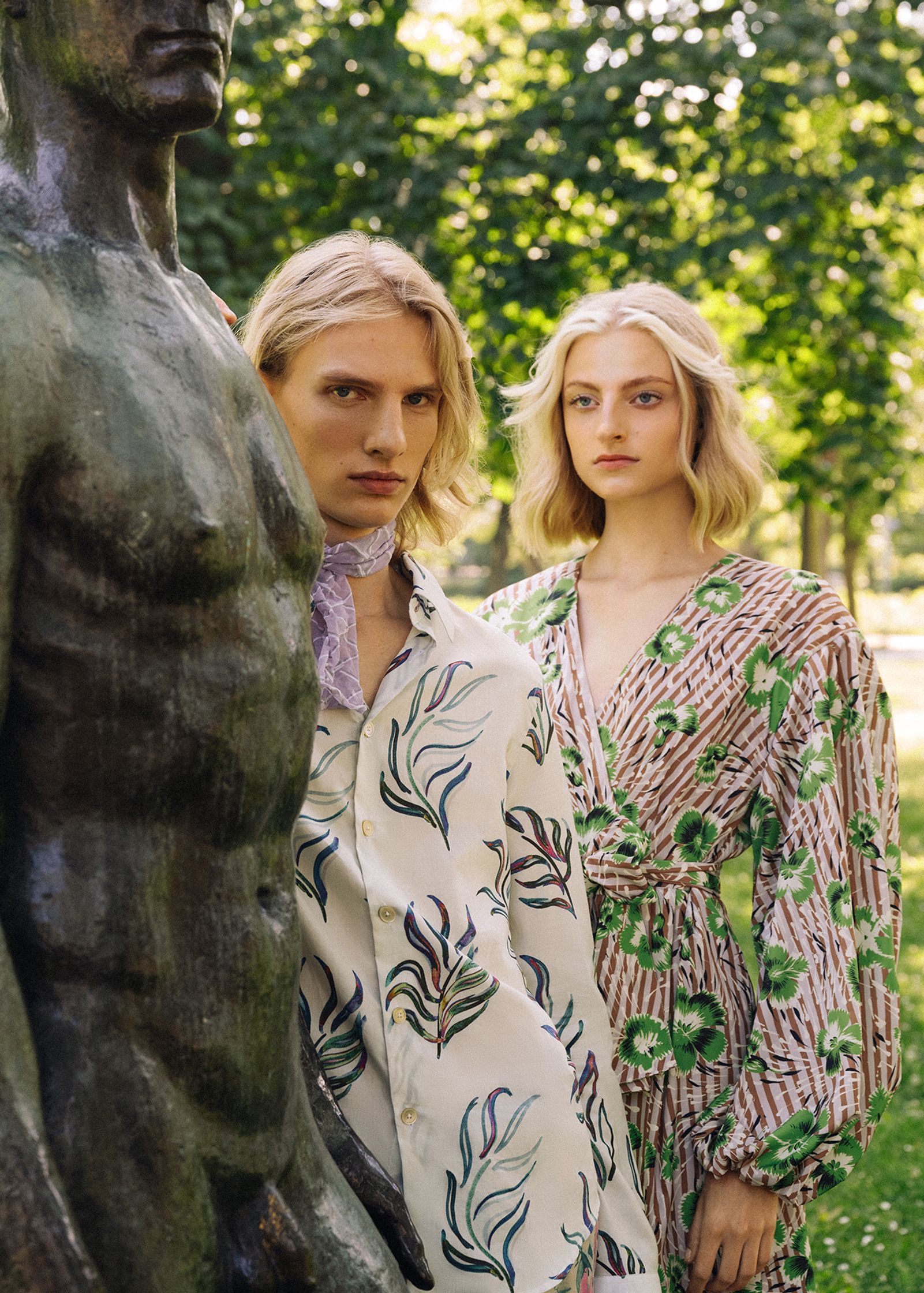 two women standing next to a statue in a park