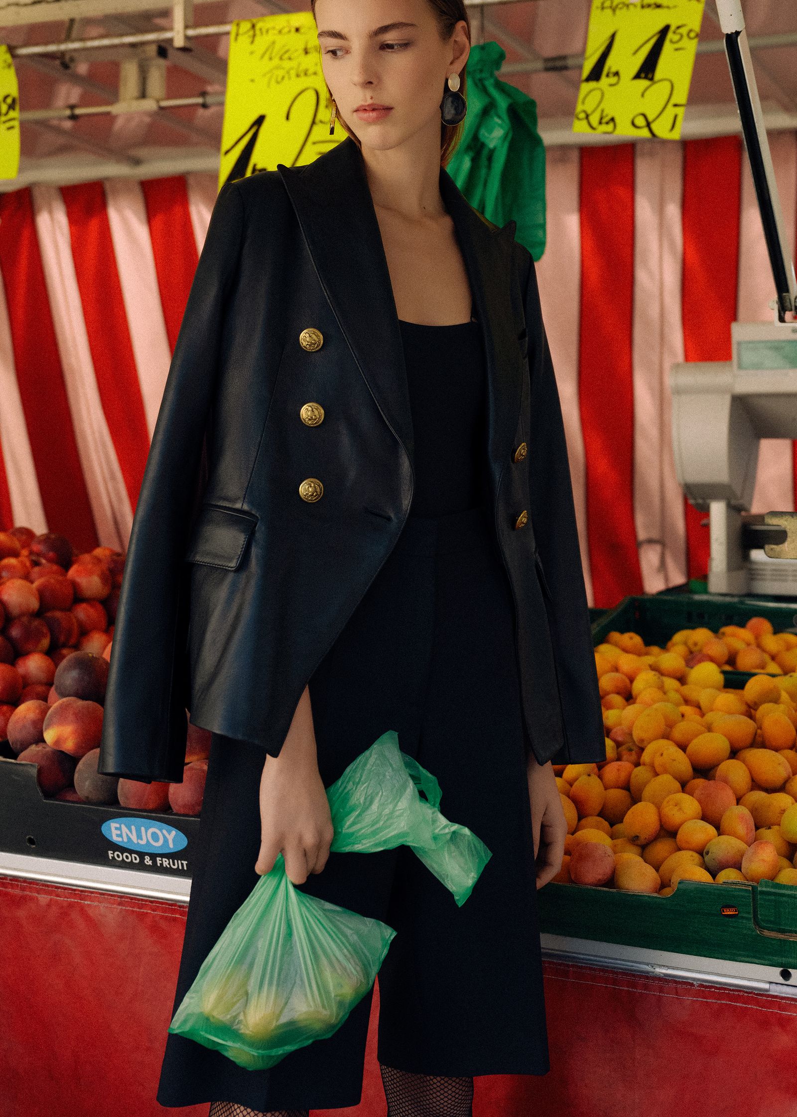 a woman in a black blazer standing in front of a fruit stand