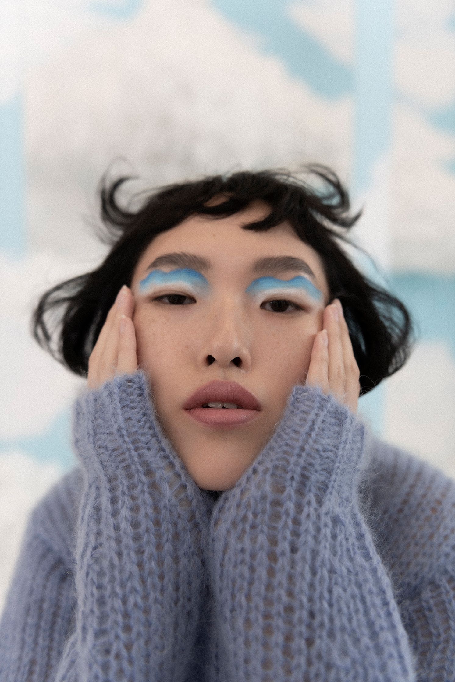 a woman with blue eye makeup posing with her hands on her face