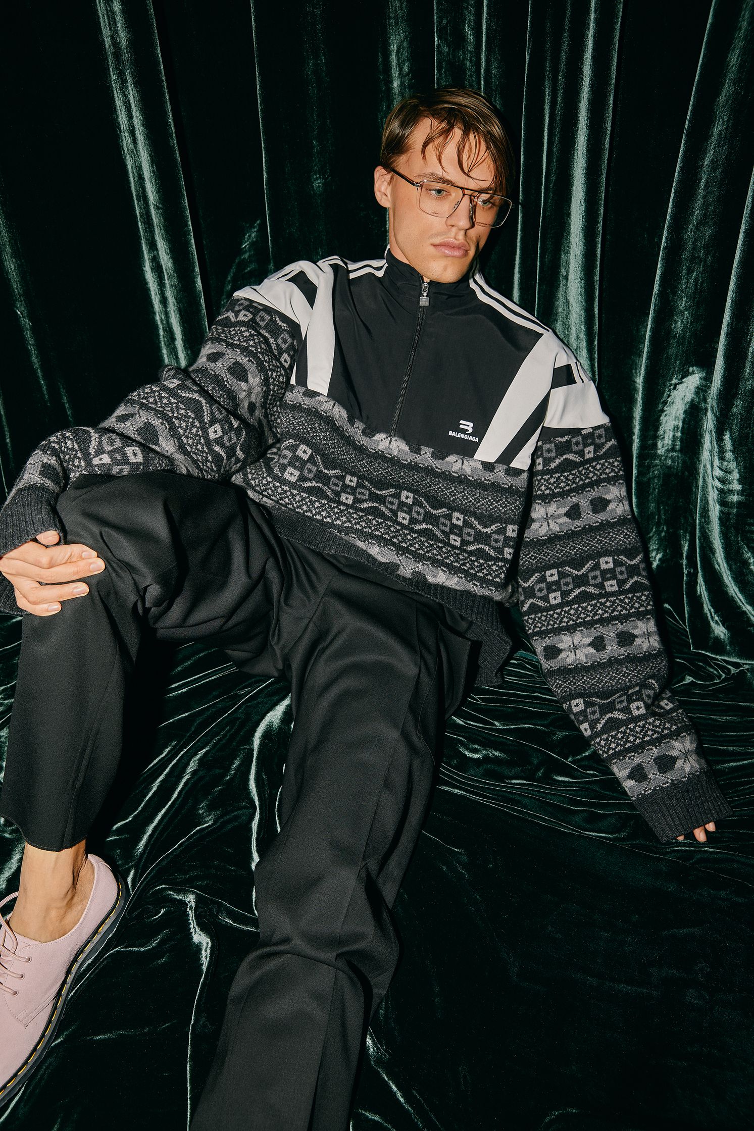 a man sitting on a velvet couch wearing a sweater and sneakers