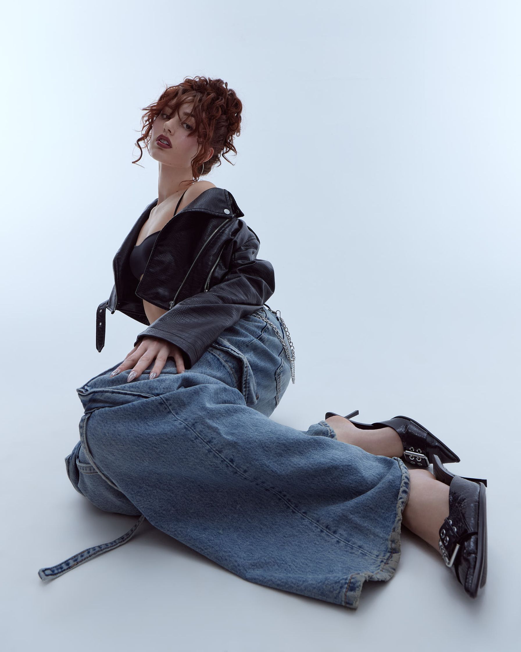 a woman sitting on the ground in jeans and a leather jacket