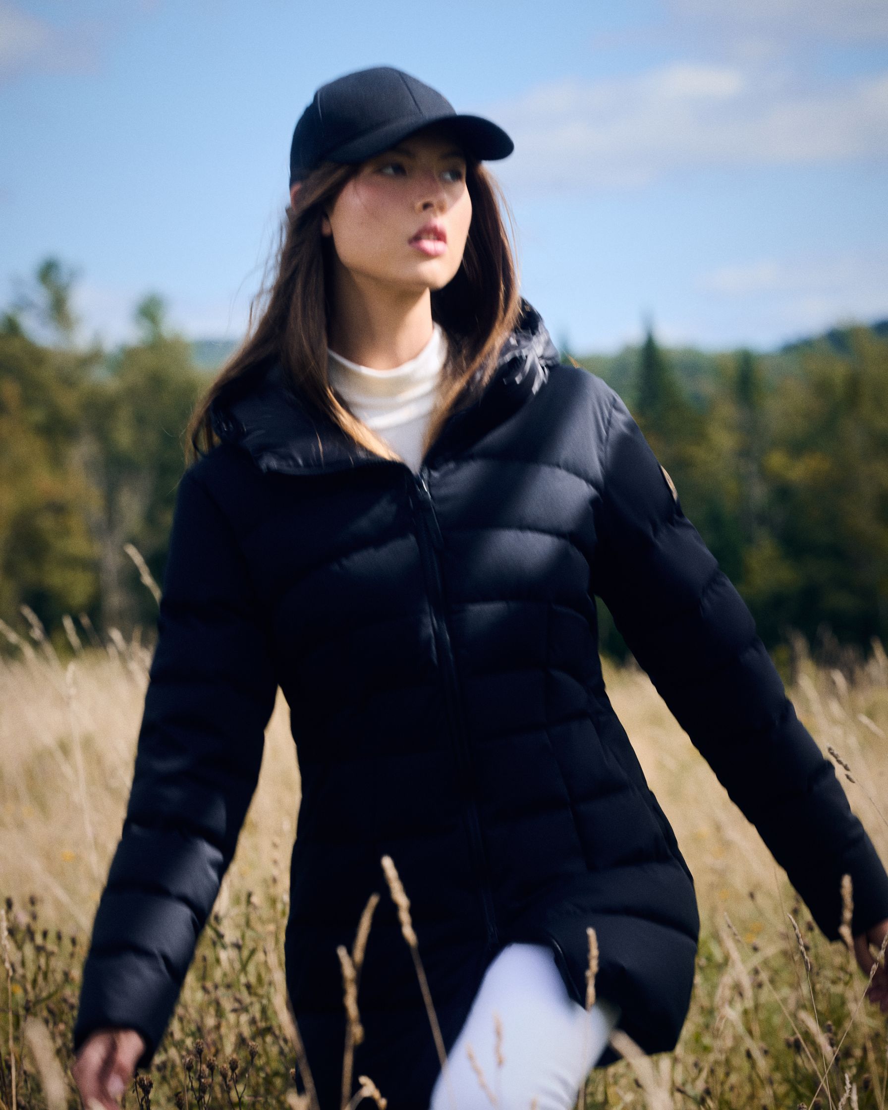 a woman in a black puffer jacket standing in a field