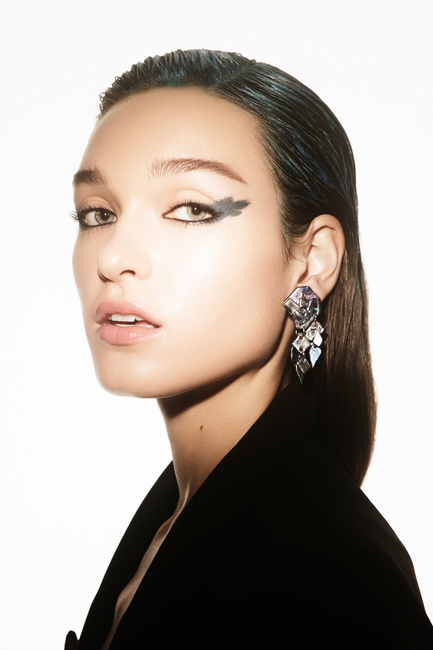 a woman with blue eyeshadow and earrings posing in front of a white background