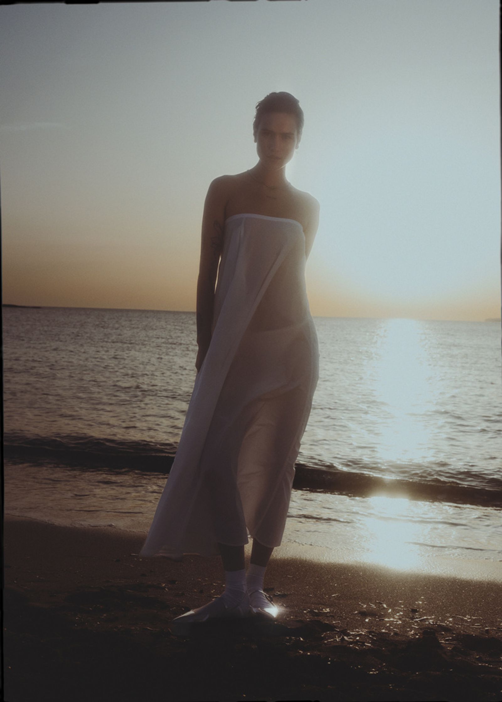 a woman in a white dress standing on the beach at sunset