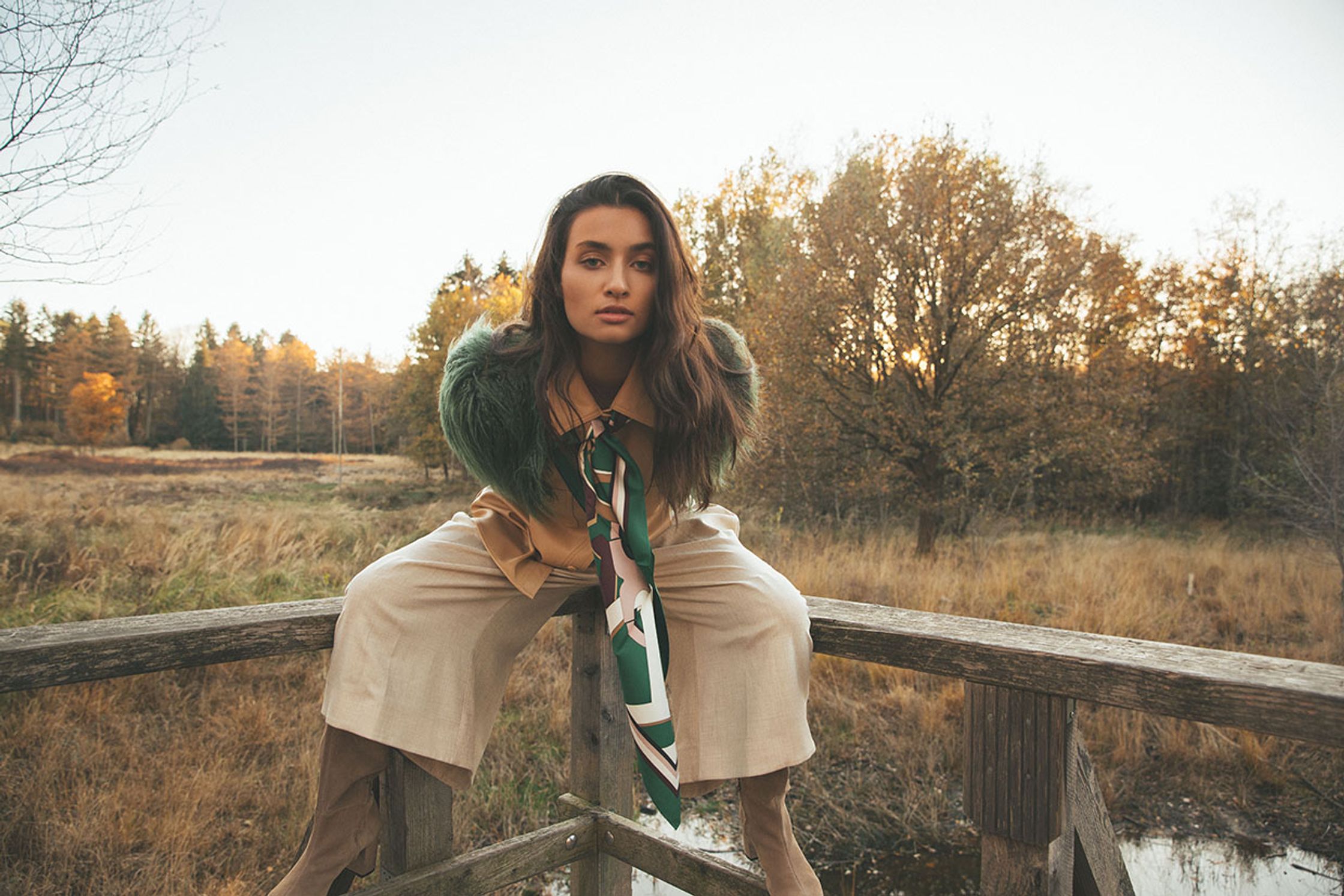 a woman is sitting on a wooden bridge in a forest