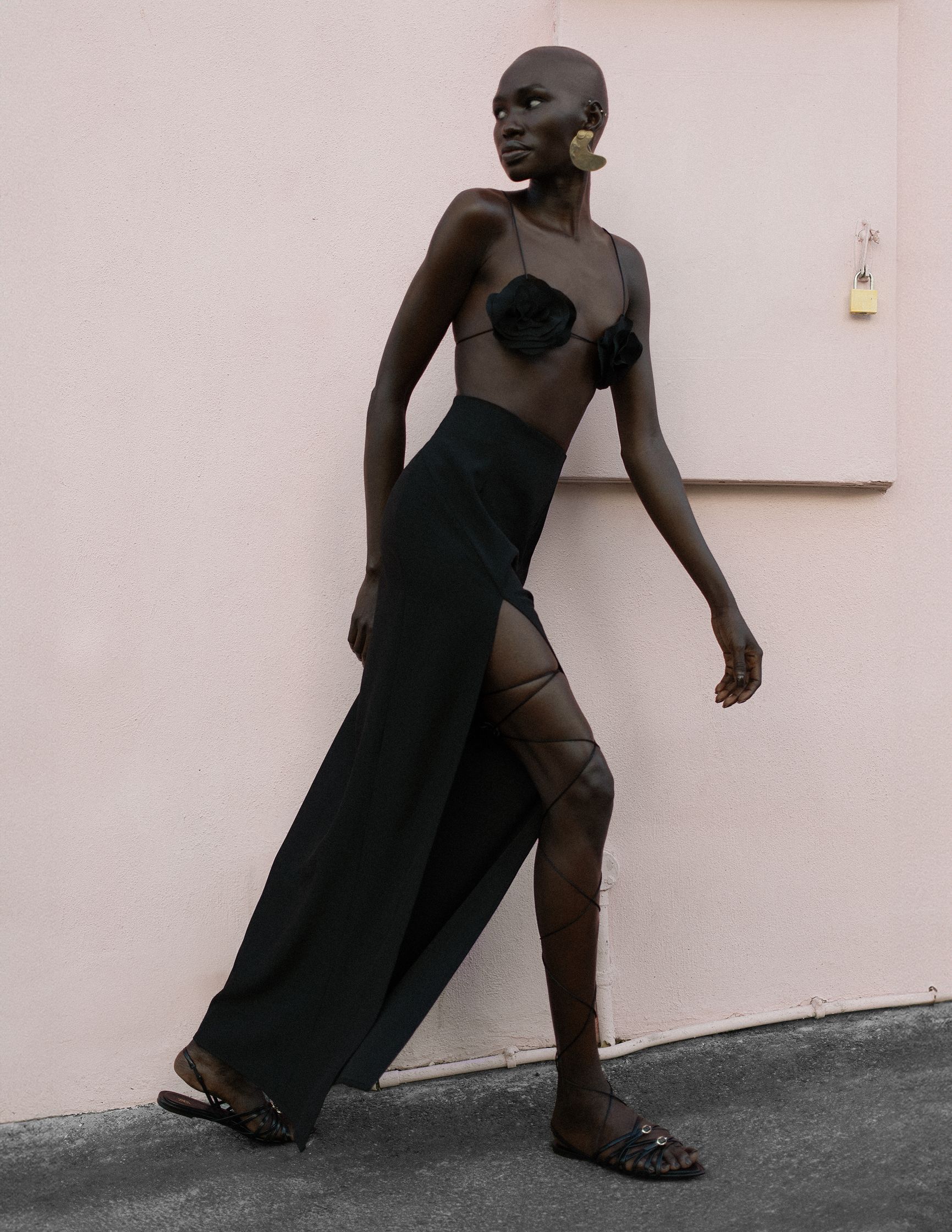a woman in a black dress and sandals is walking in front of a pink wall