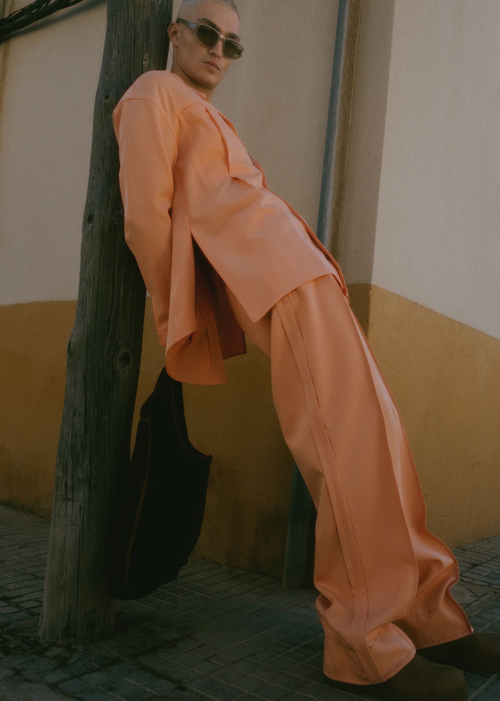 a man in an orange suit leaning against a pole