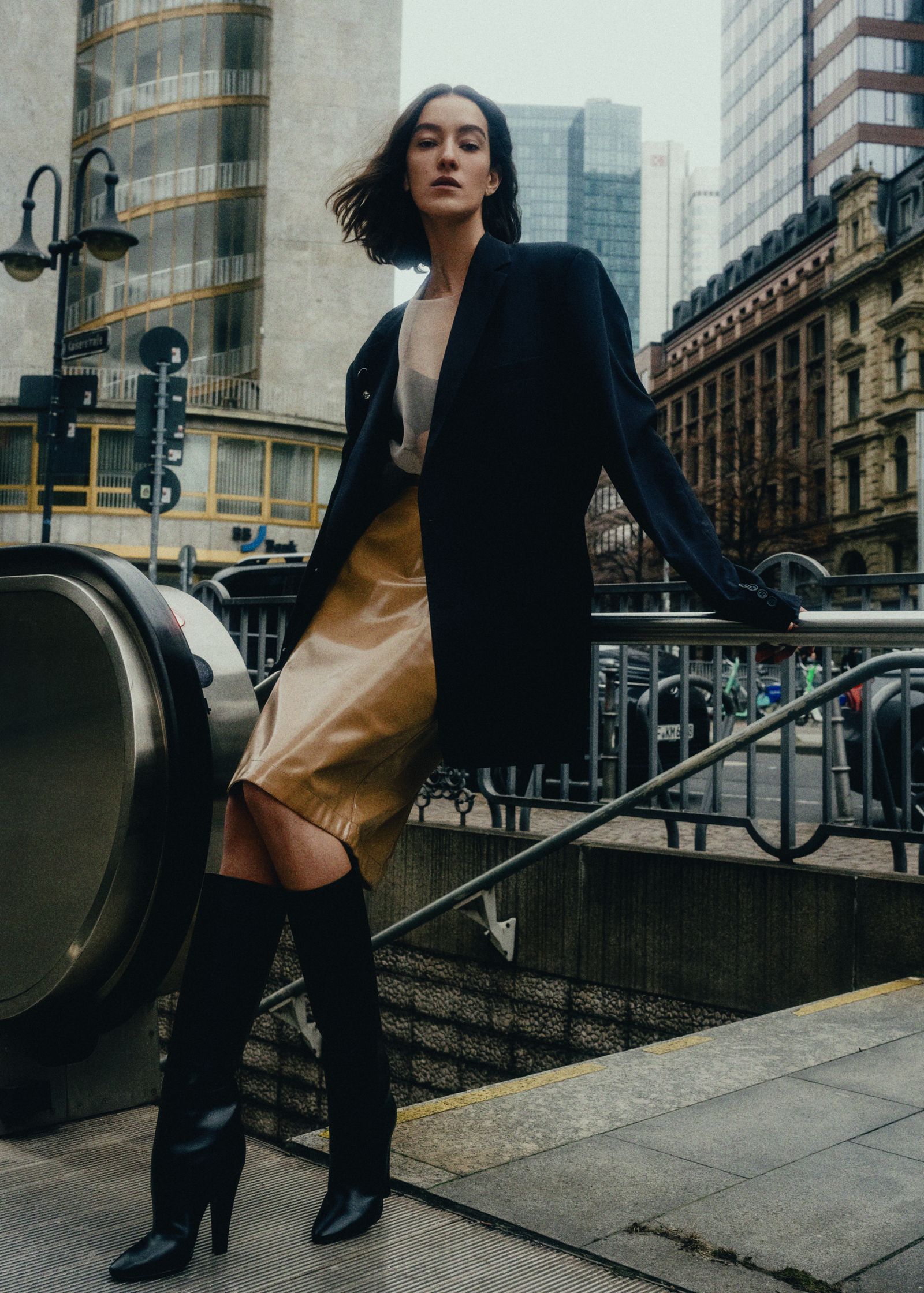 a woman in a black coat and gold skirt posing on a railing