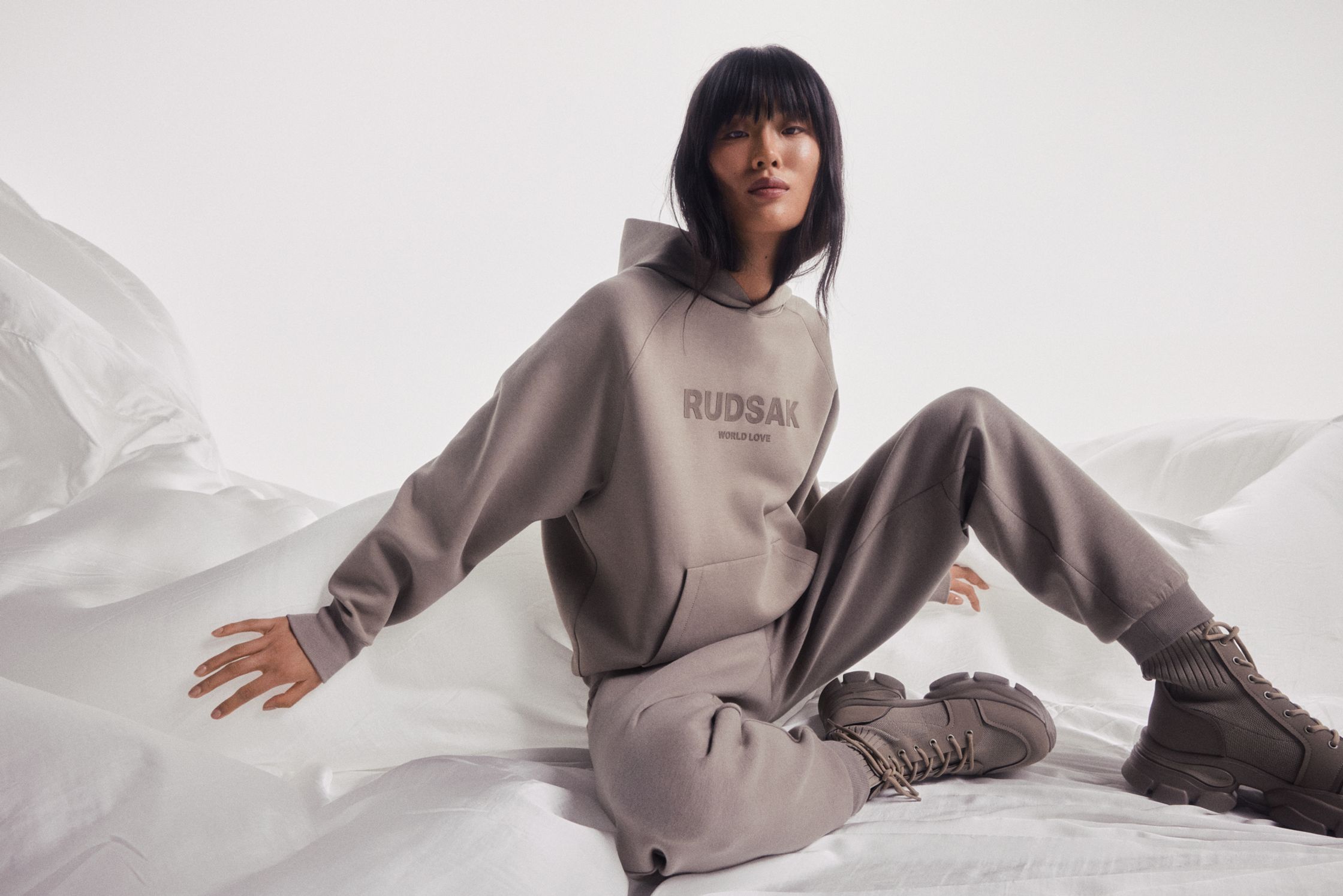 a woman in a grey hoodie sitting on top of a white sheet