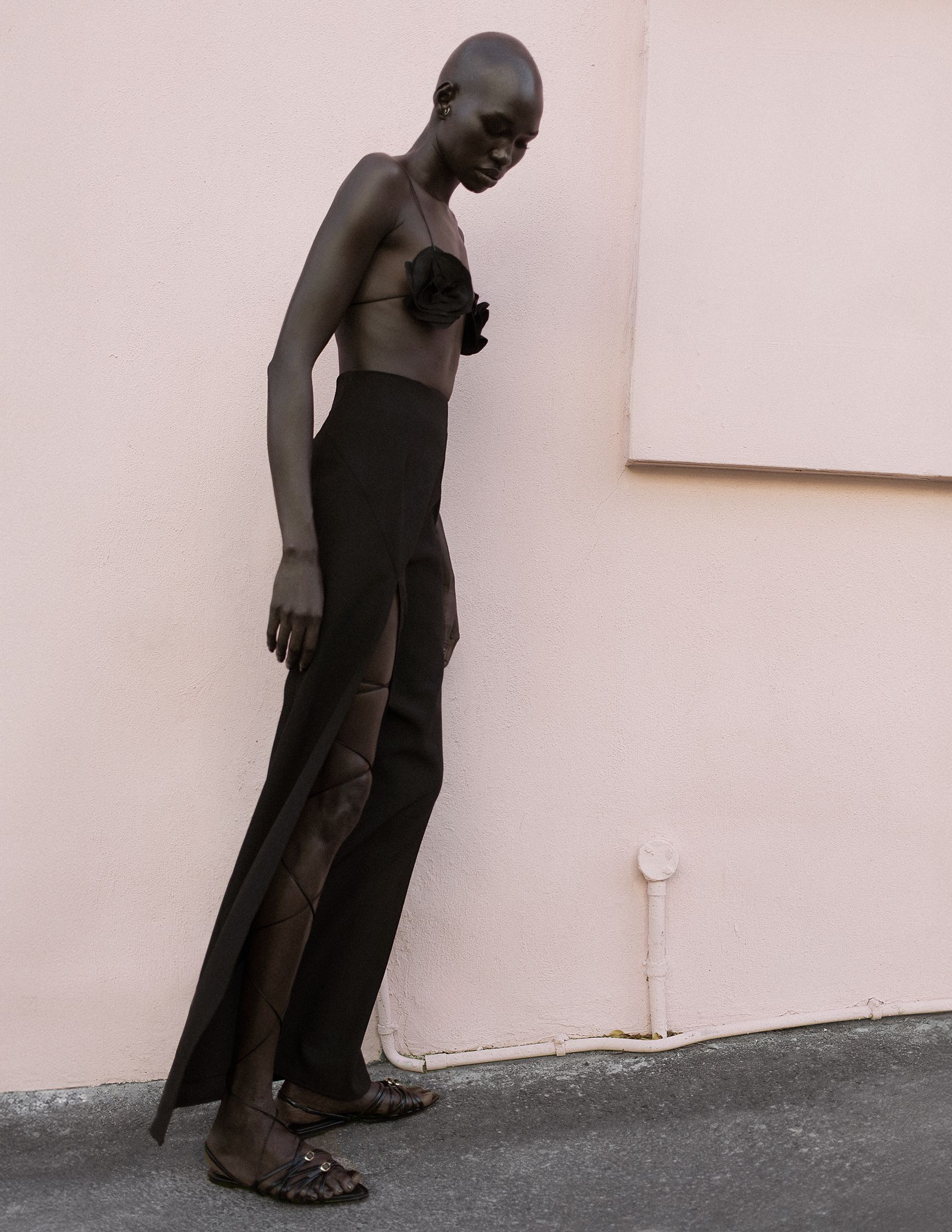 a woman in a black dress leaning against a pink wall