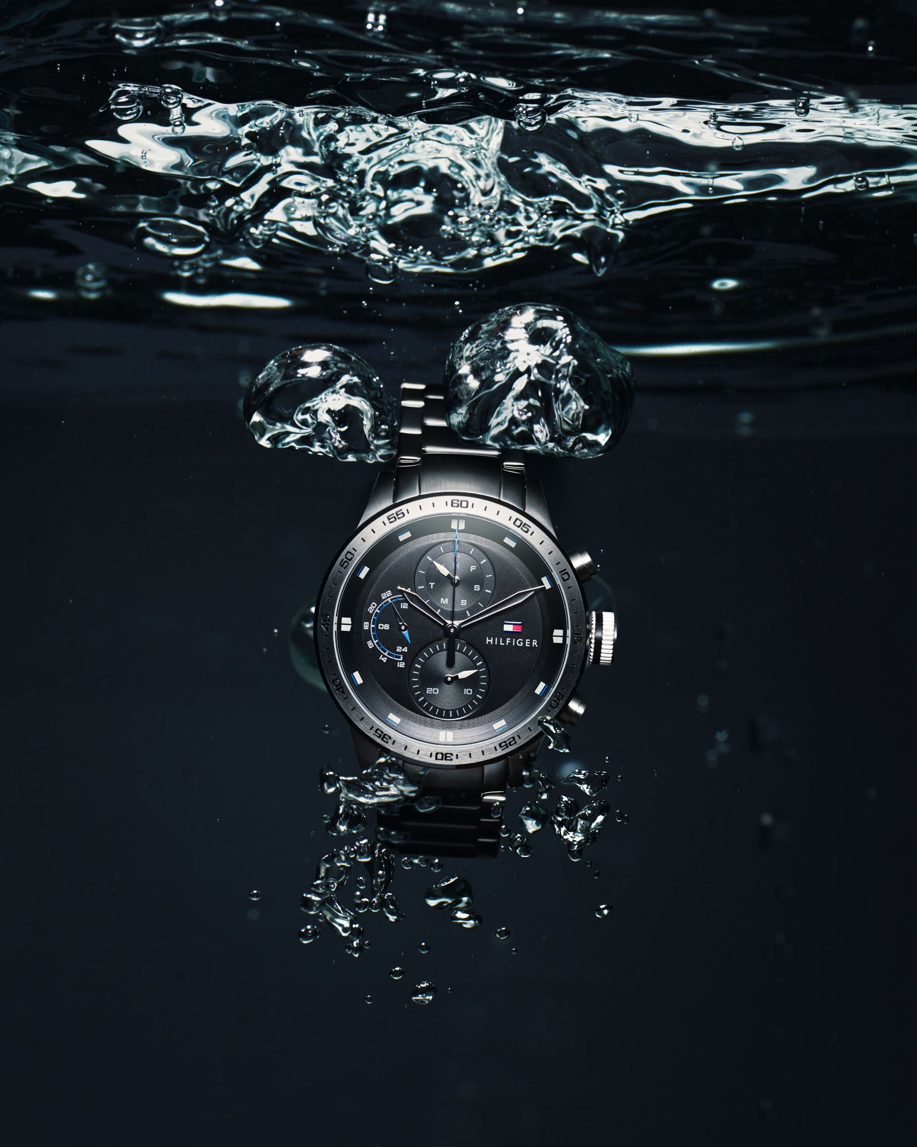 Tommy Hilfiger luxury watch submerged in water, surrounded by abstract bubbles and splashes.