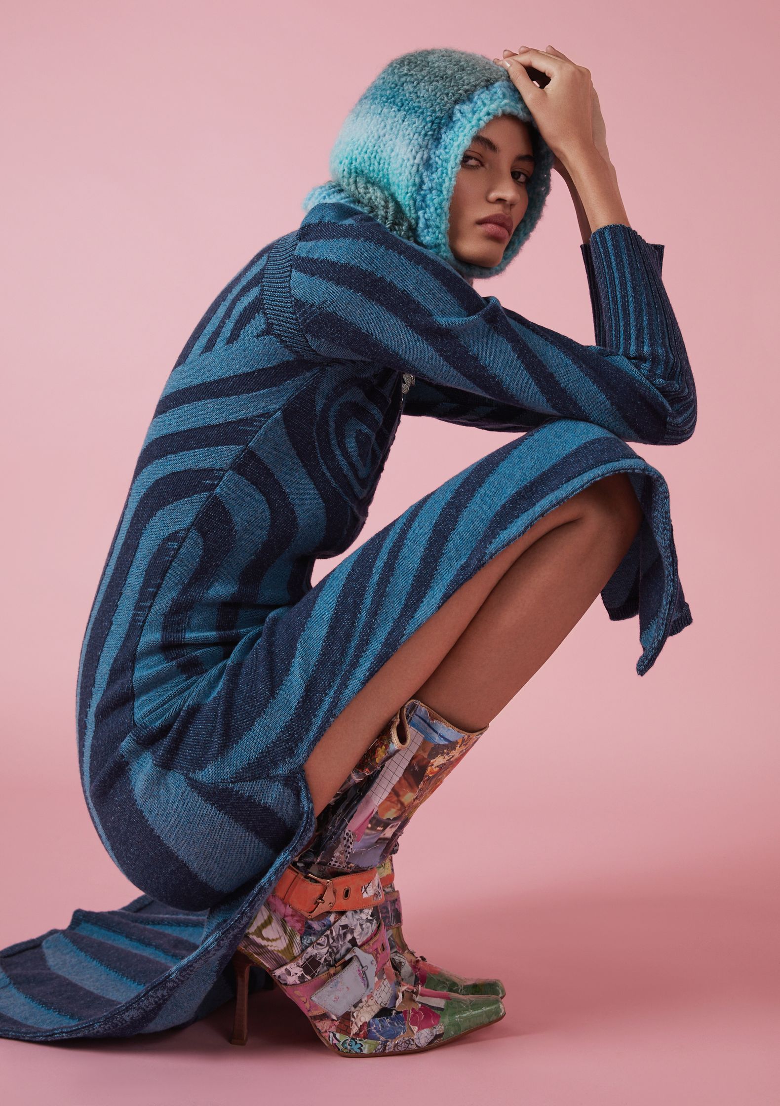 a woman in a blue dress and colorful boots crouching on a pink background