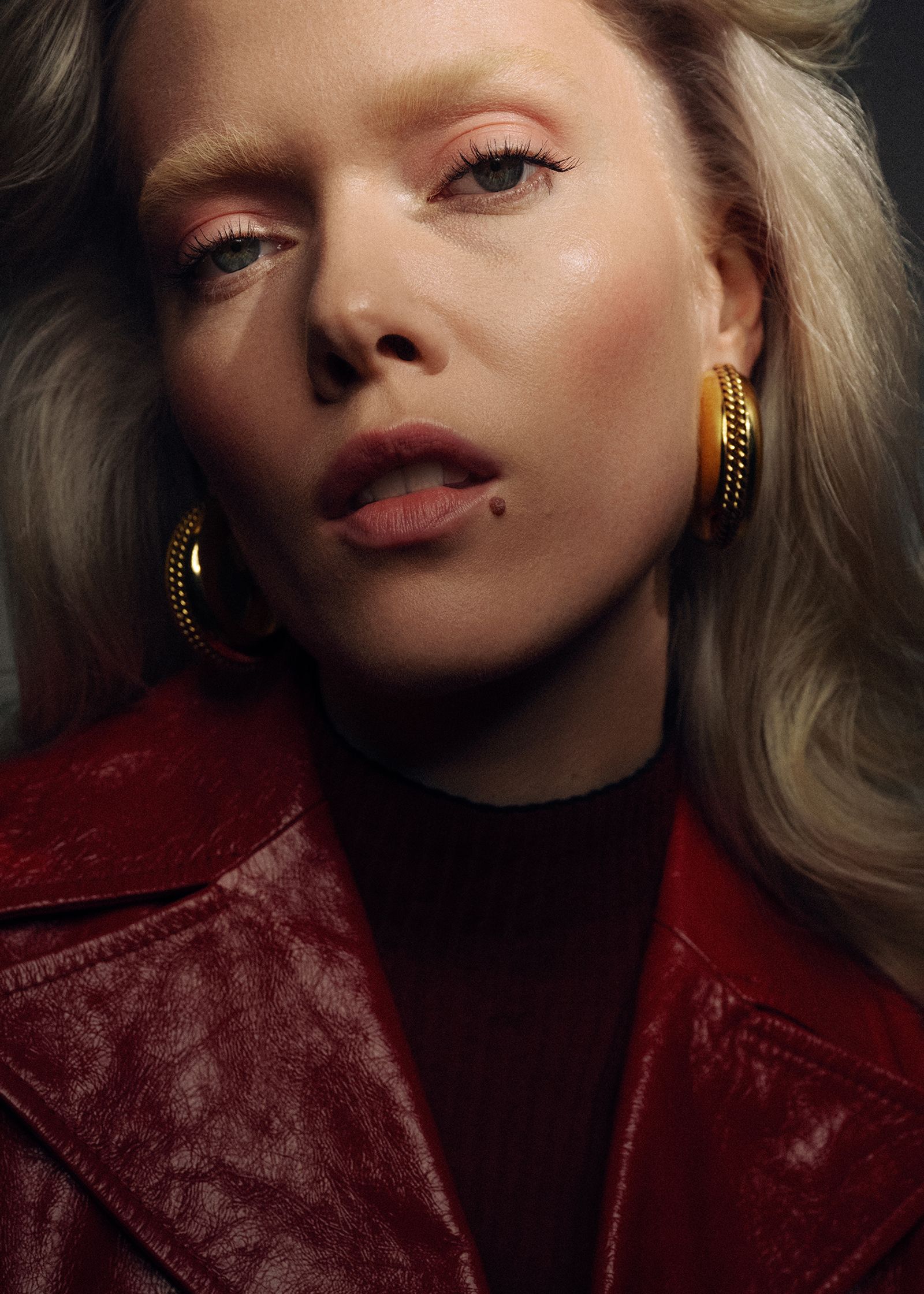 a blonde woman wearing a red jacket and gold earrings