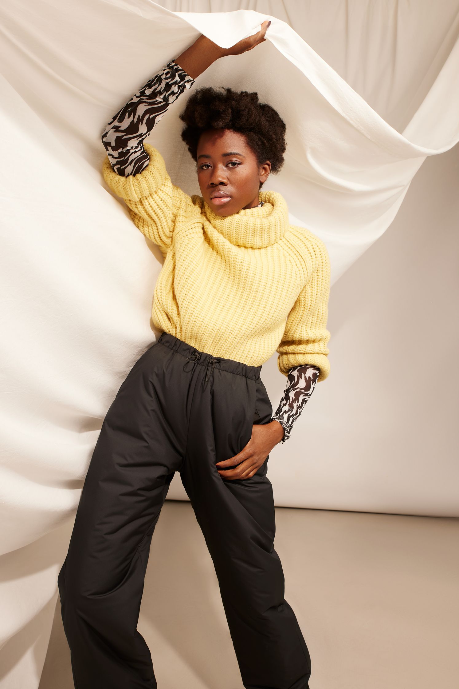 a black woman wearing a yellow sweater and black pants