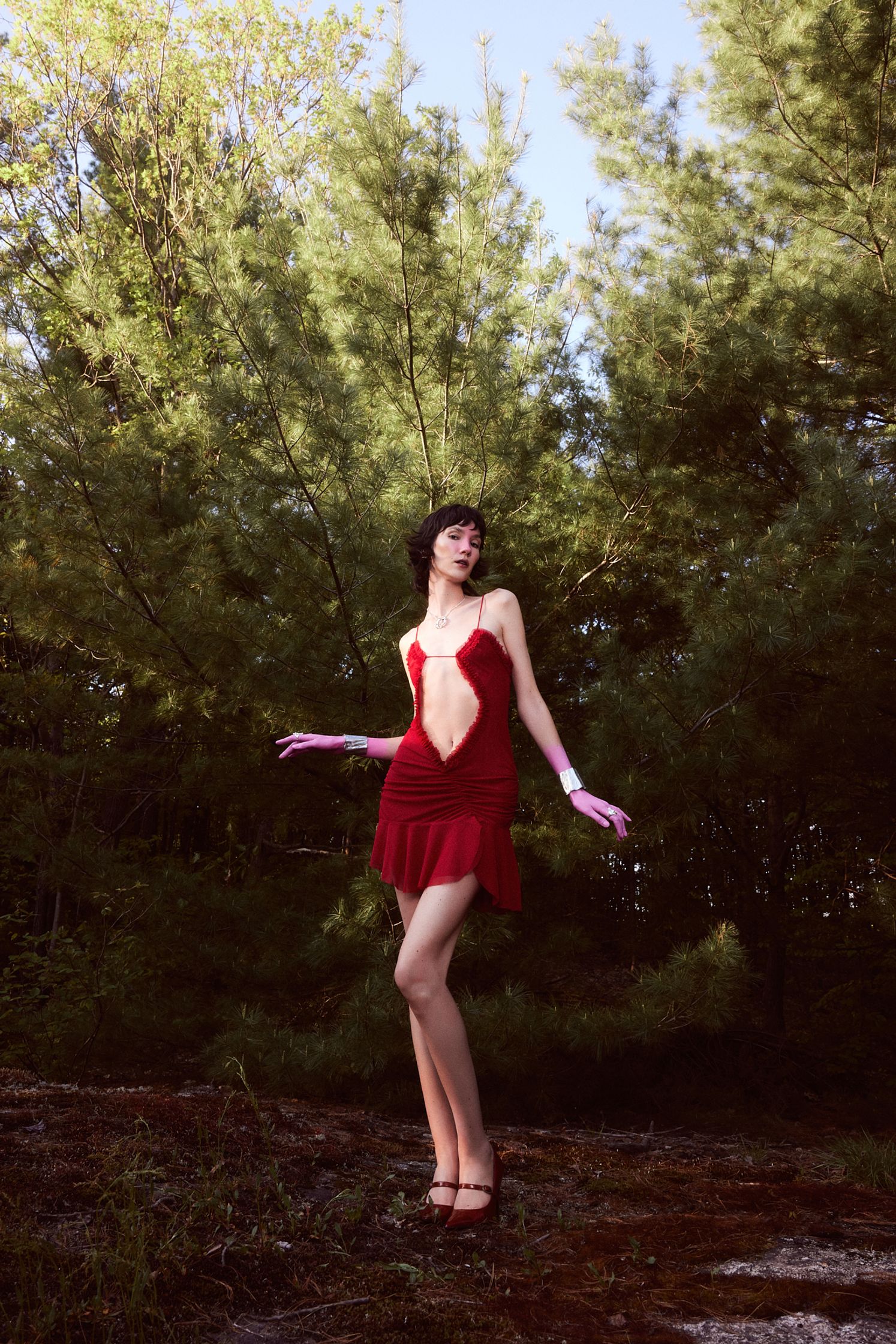 a woman in a red dress is standing in the woods