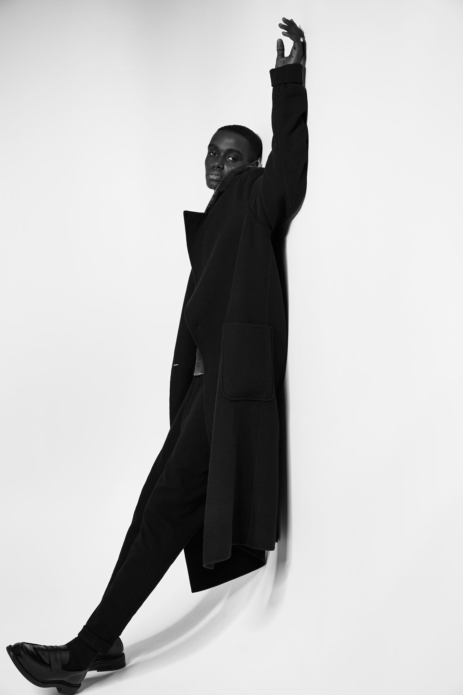 a man in a black coat leaning against a wall