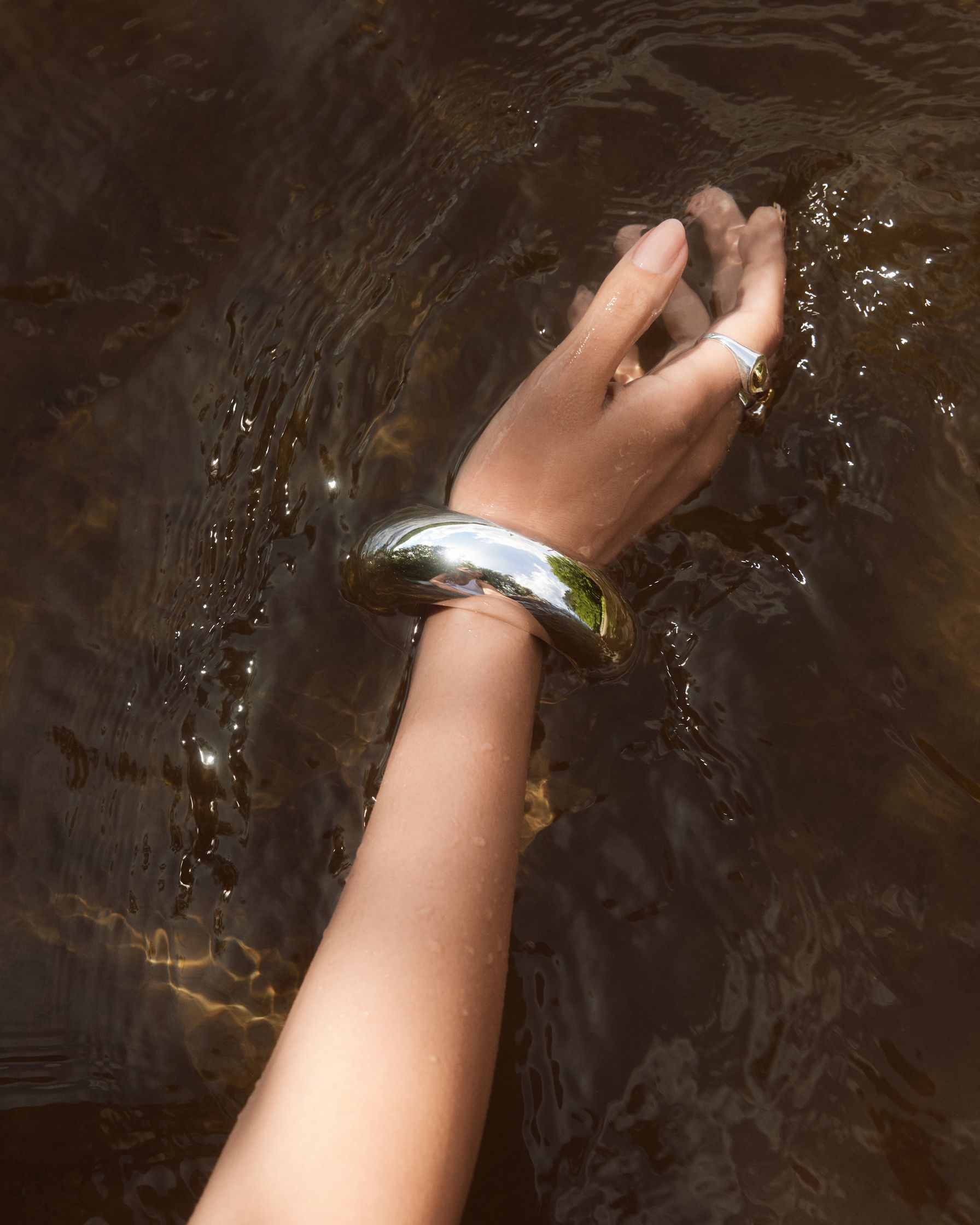 a woman's hand in the water with a silver bangle