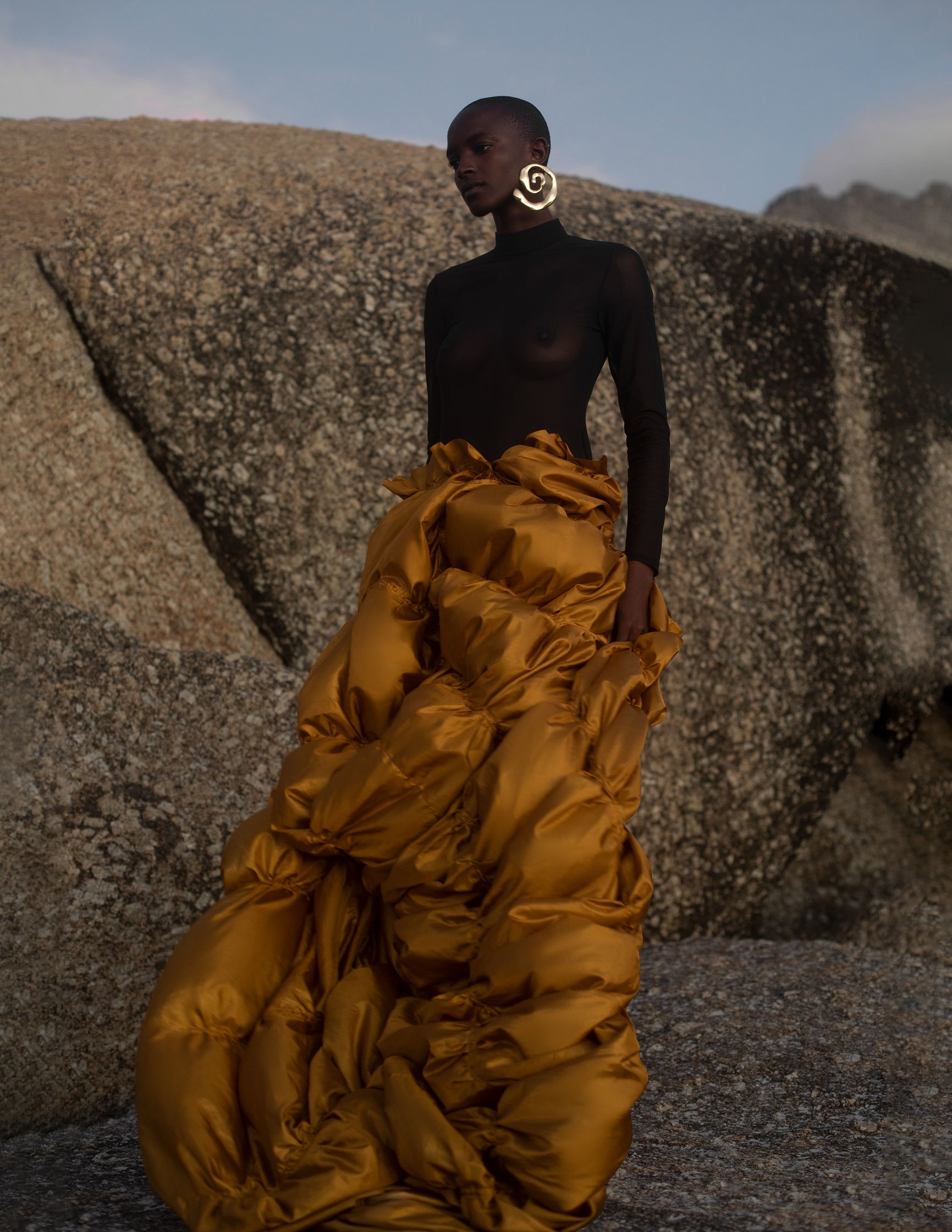 a black woman in a gold skirt standing on a rock