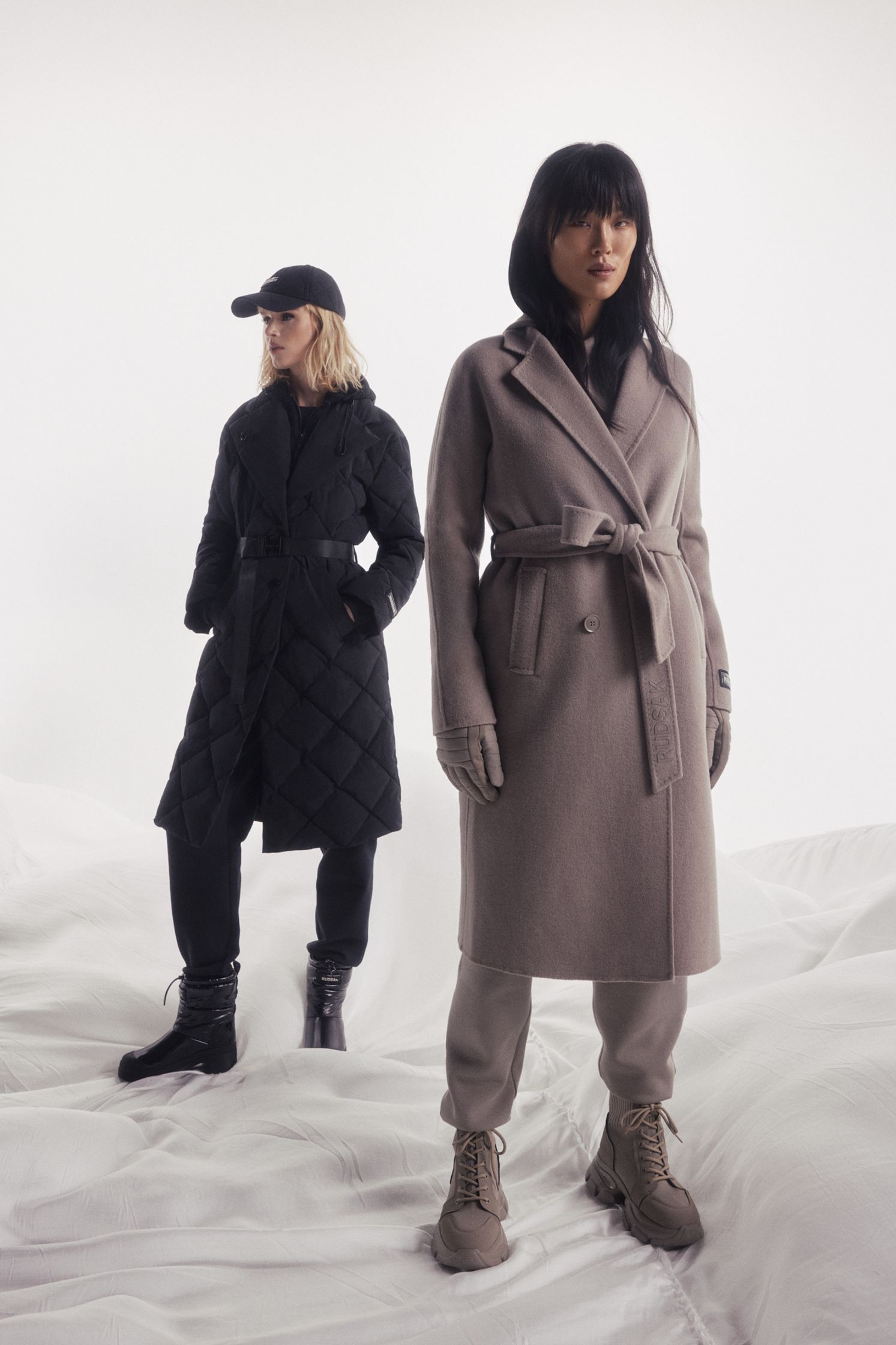 two women in coats standing on a bed