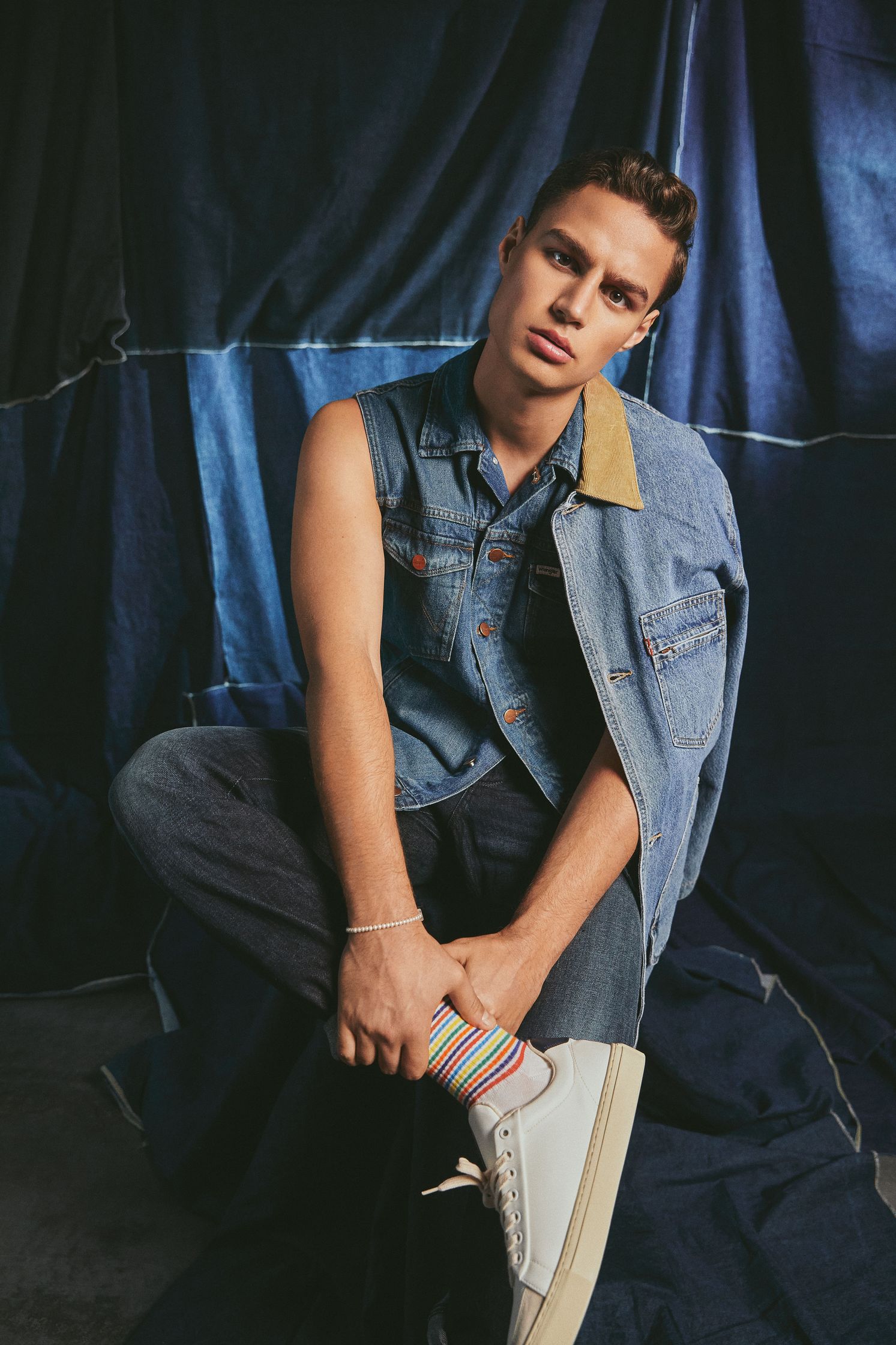 a young man wearing a denim vest and sneakers
