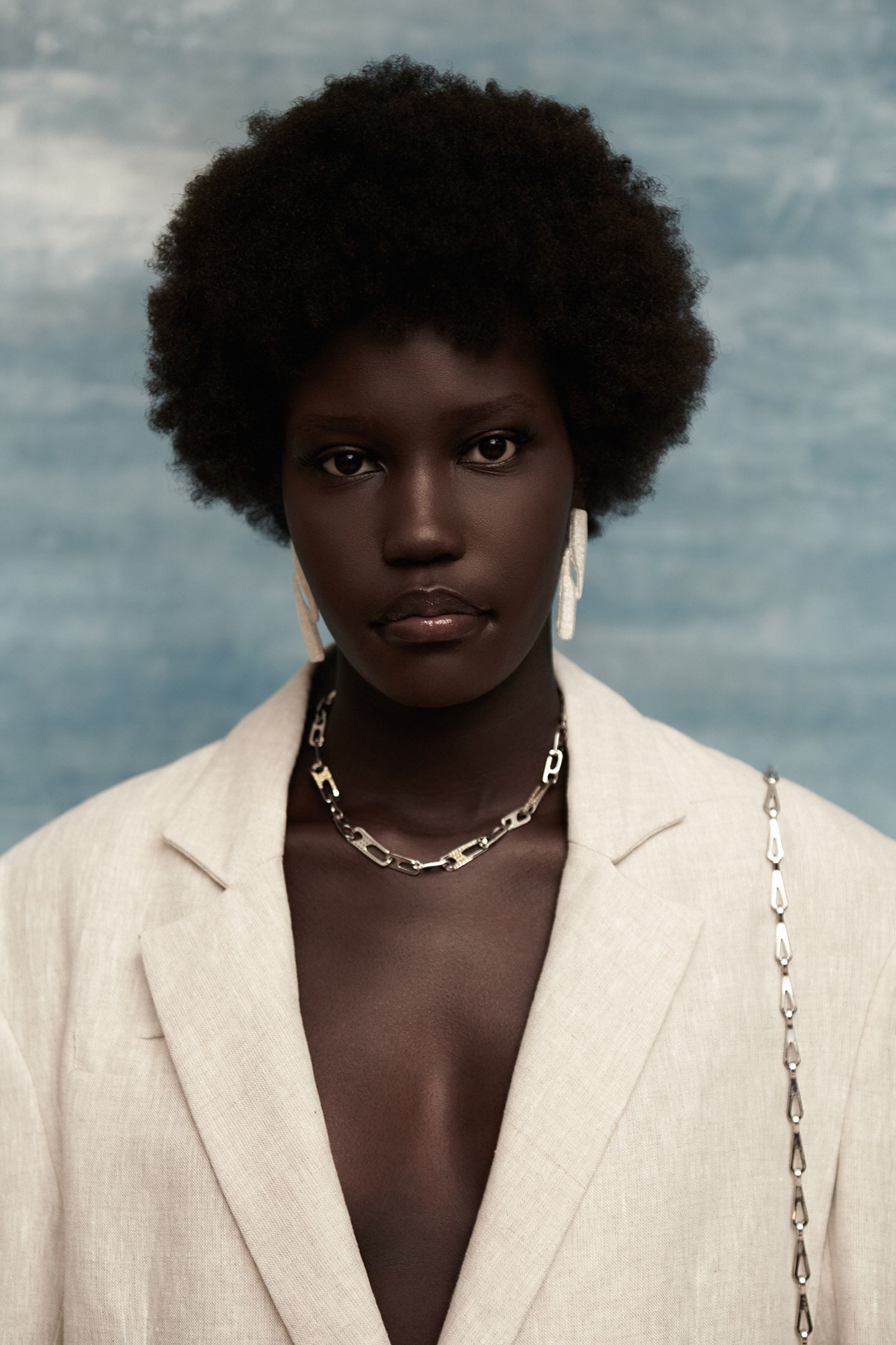 a black woman in a white blazer and chain necklace