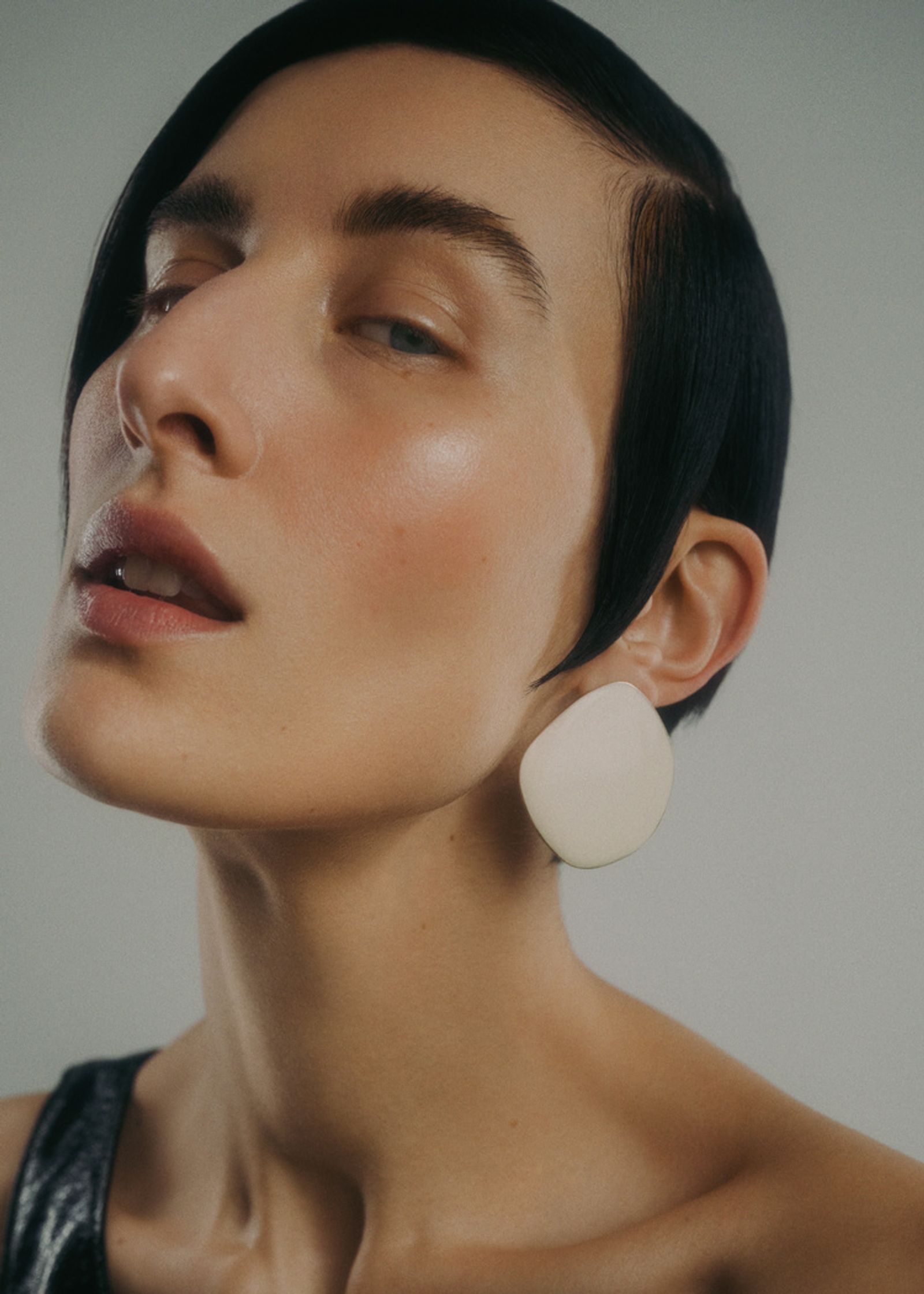 a woman wearing a black top and white earrings