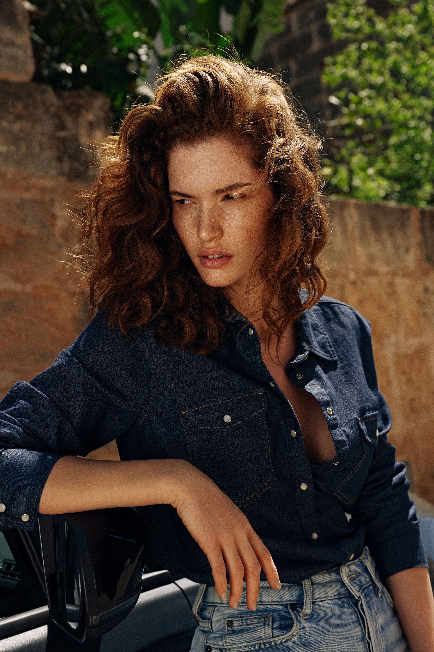 a woman in a denim shirt leaning against a car