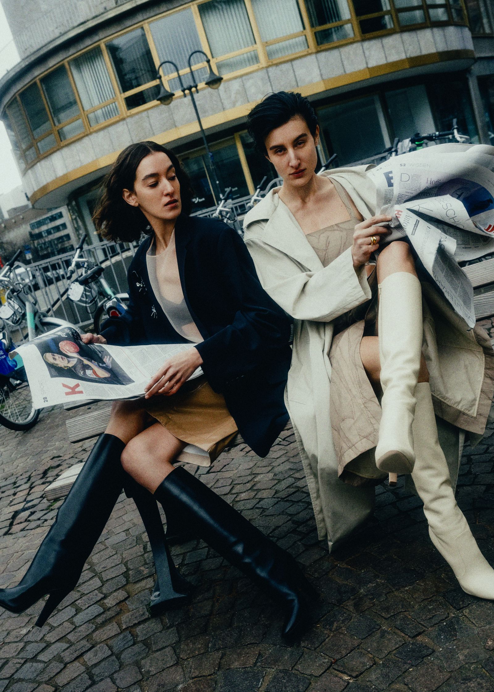 two women sitting on a bench reading a magazine