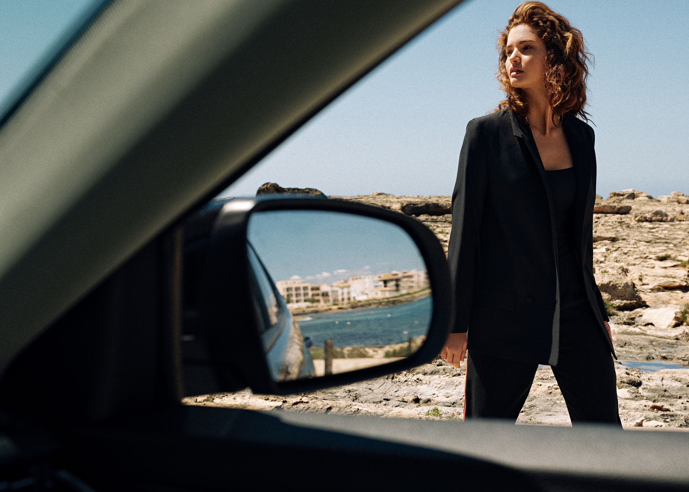 a woman in a black suit standing next to a car
