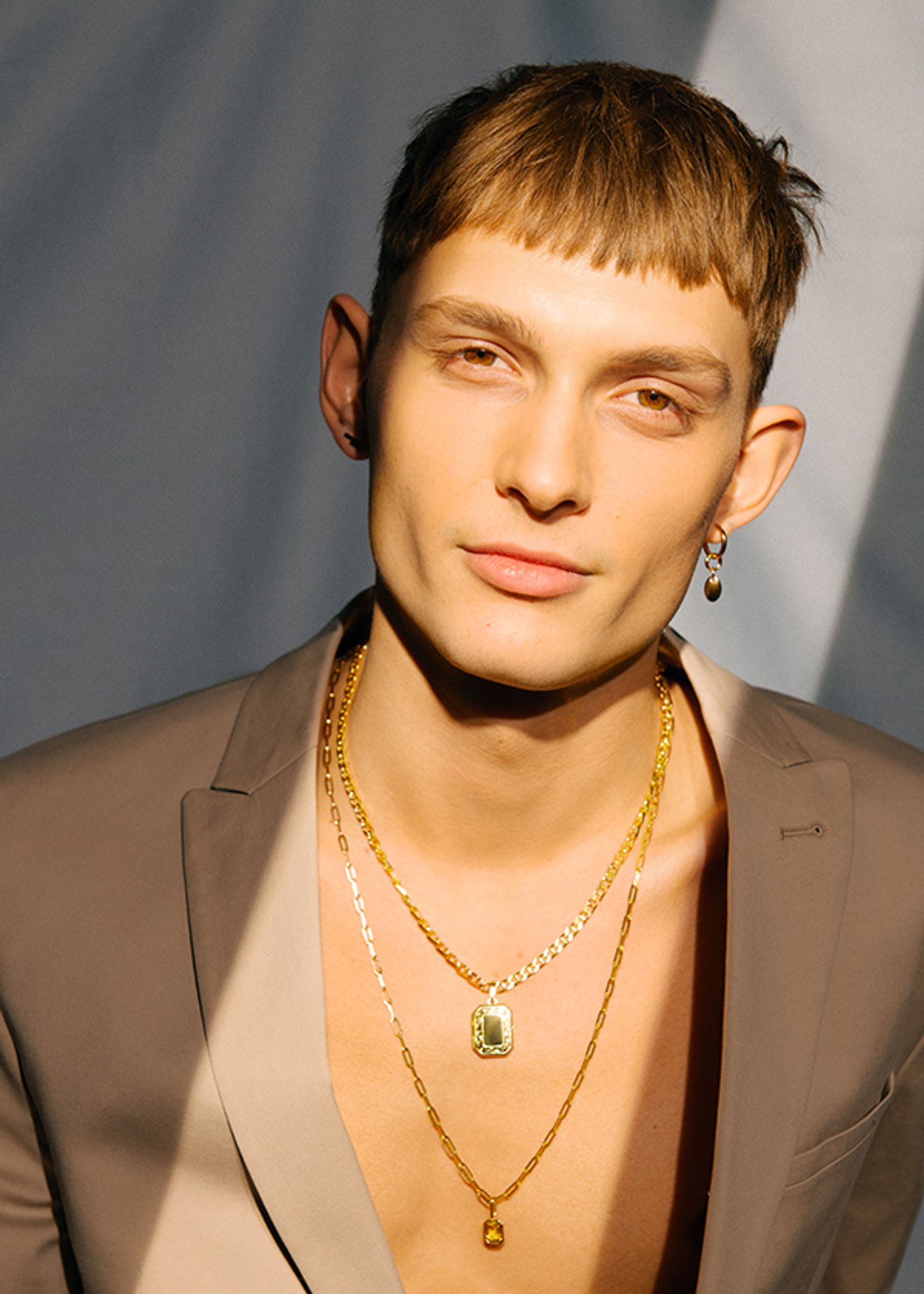 a man in a tan suit with gold necklaces