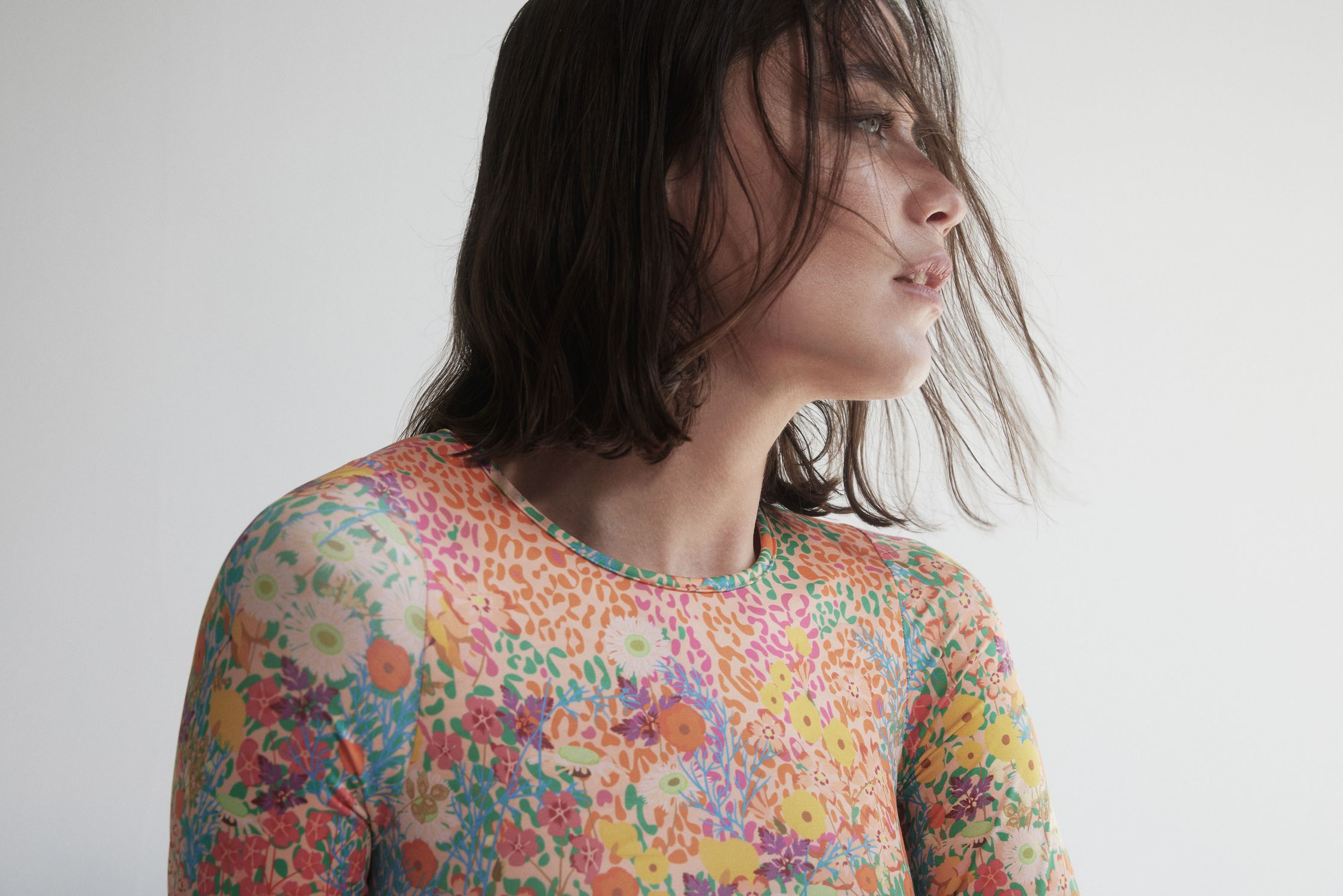 a woman in a colorful floral top leaning against a wall