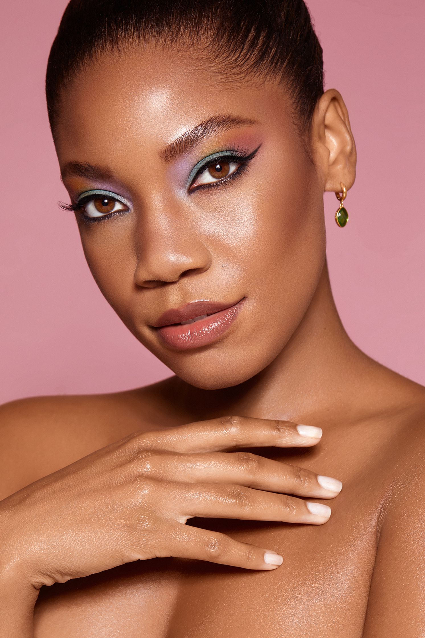 a black woman with colorful makeup posing on a pink background