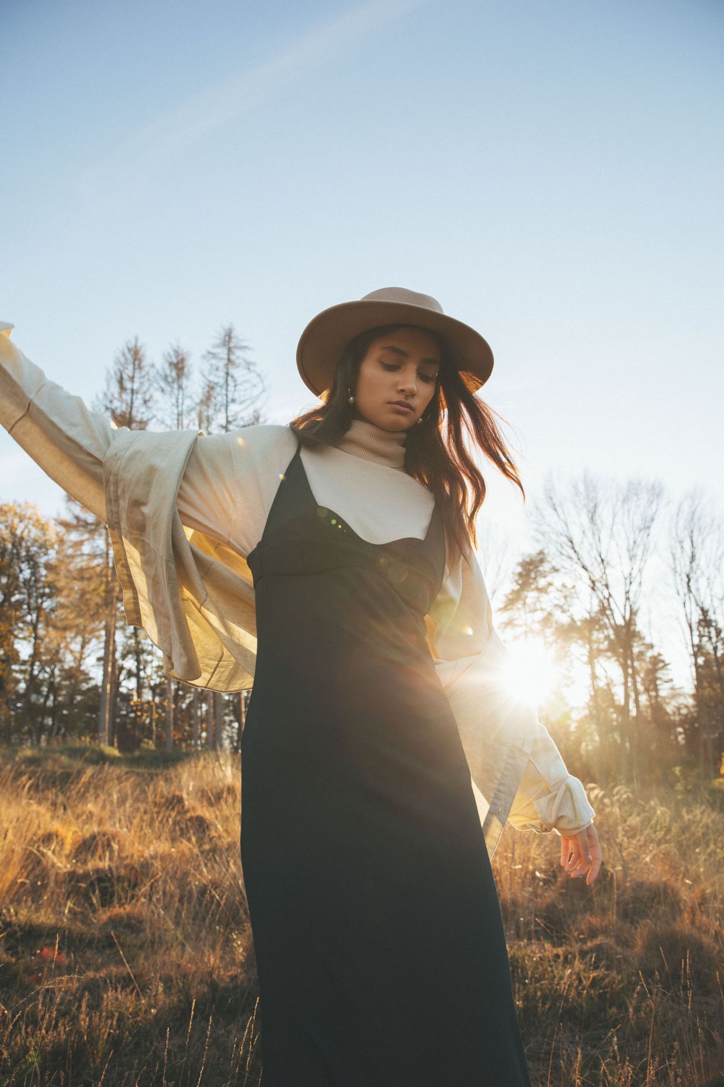 a woman in a long dress and hat standing in a field