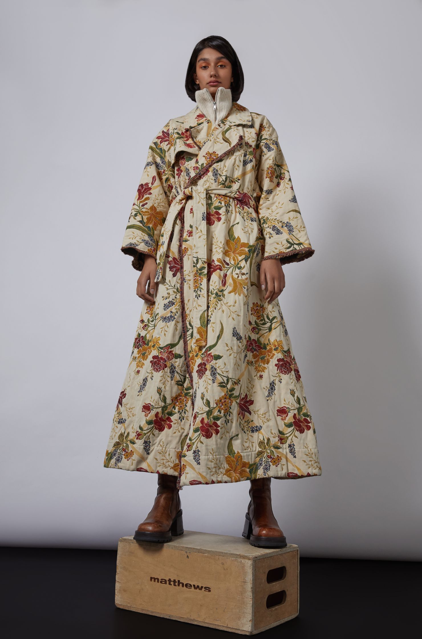 a woman wearing a floral printed coat standing on a wooden box