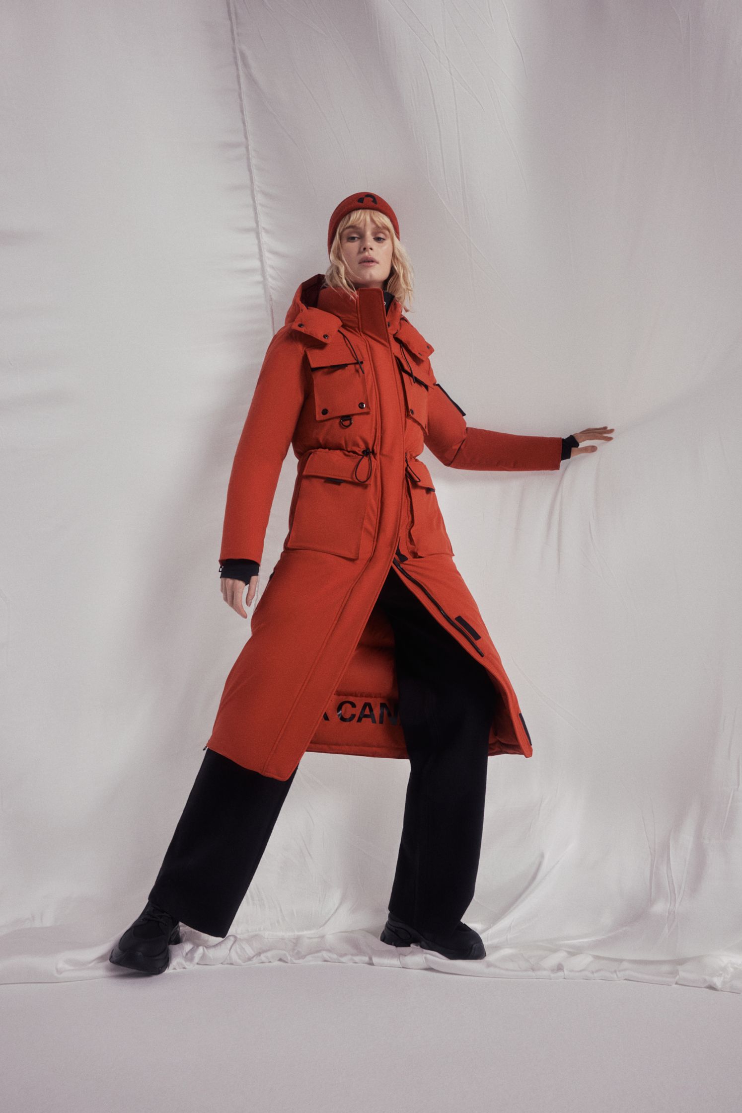 a woman in a red coat posing on a white sheet