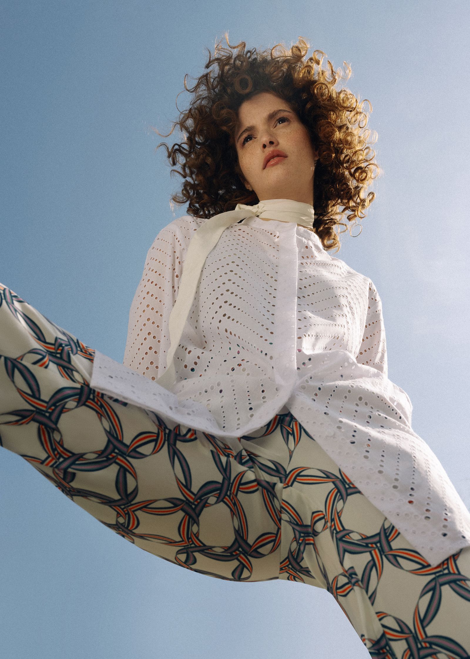 a woman with curly hair in a white shirt and patterned pants