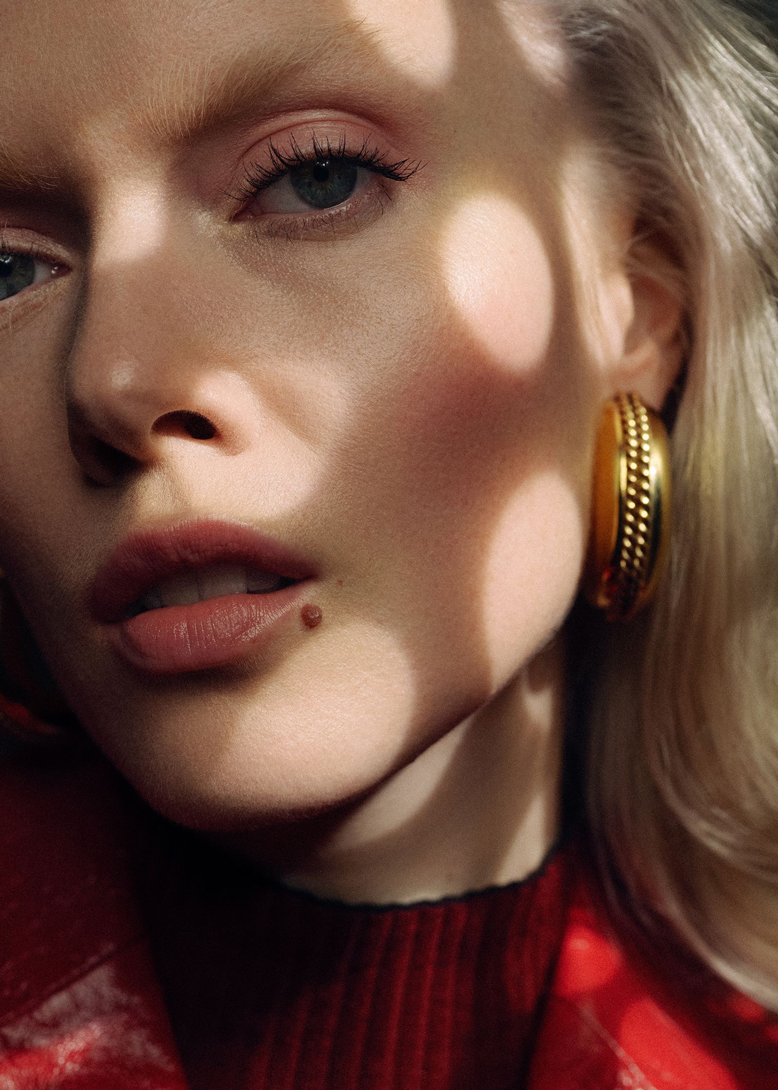 a blonde woman in a red jacket with gold hoop earrings
