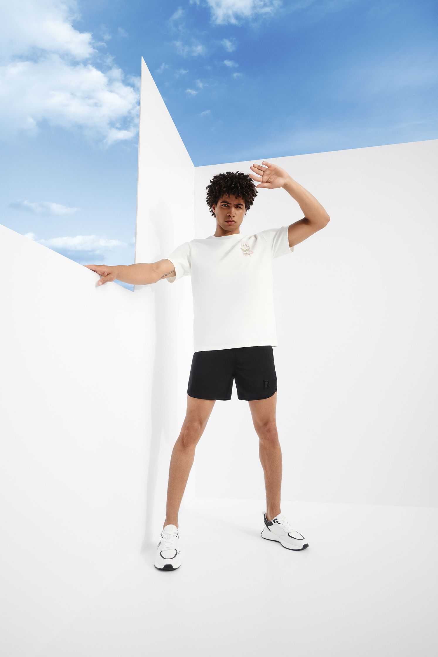 a man in a white t - shirt and black shorts is posing in front of a white wall