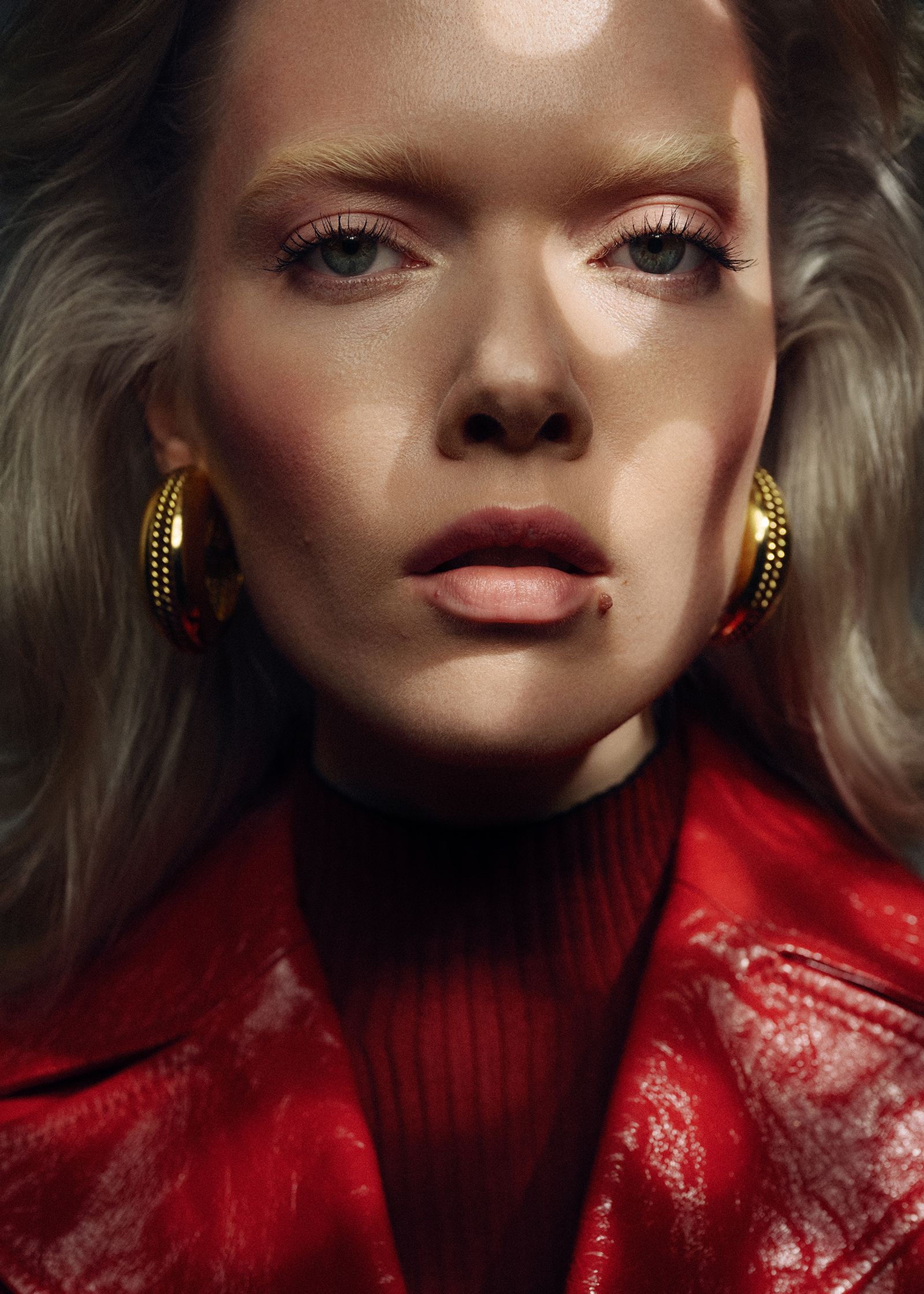 a blonde woman in a red jacket and gold earrings