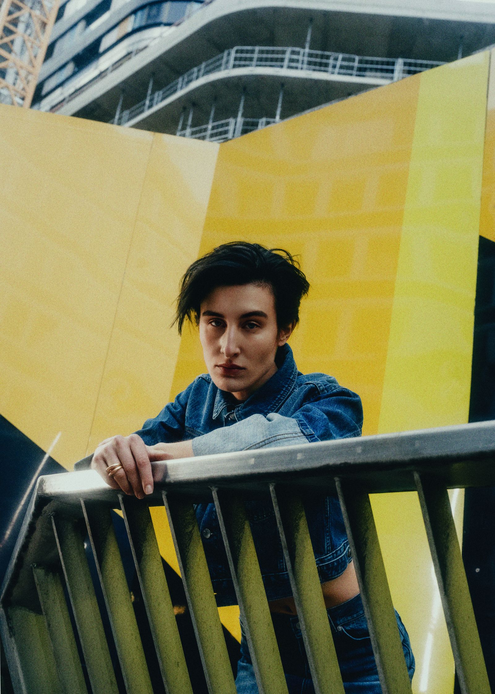 a woman in a denim jacket leaning against a railing