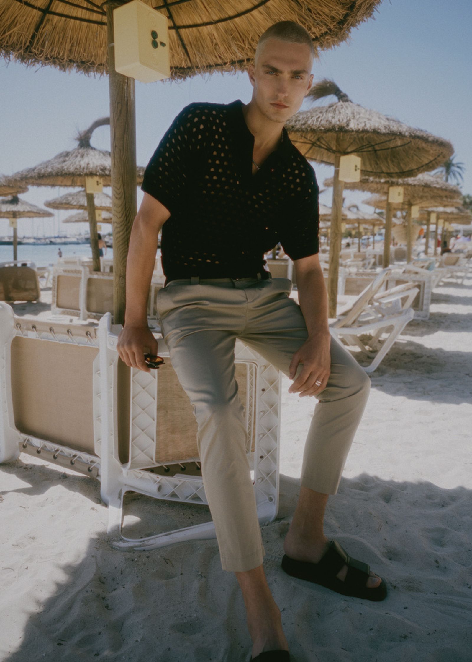 a man sitting on a beach in a tan shirt and khaki pants