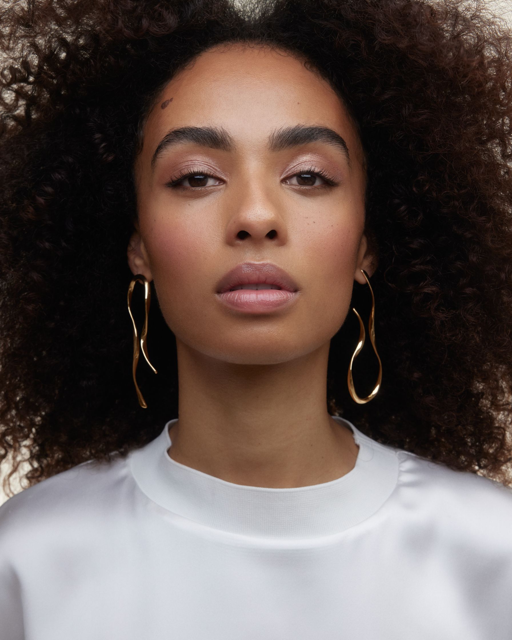 a woman with curly hair wearing a white shirt and gold hoop earrings
